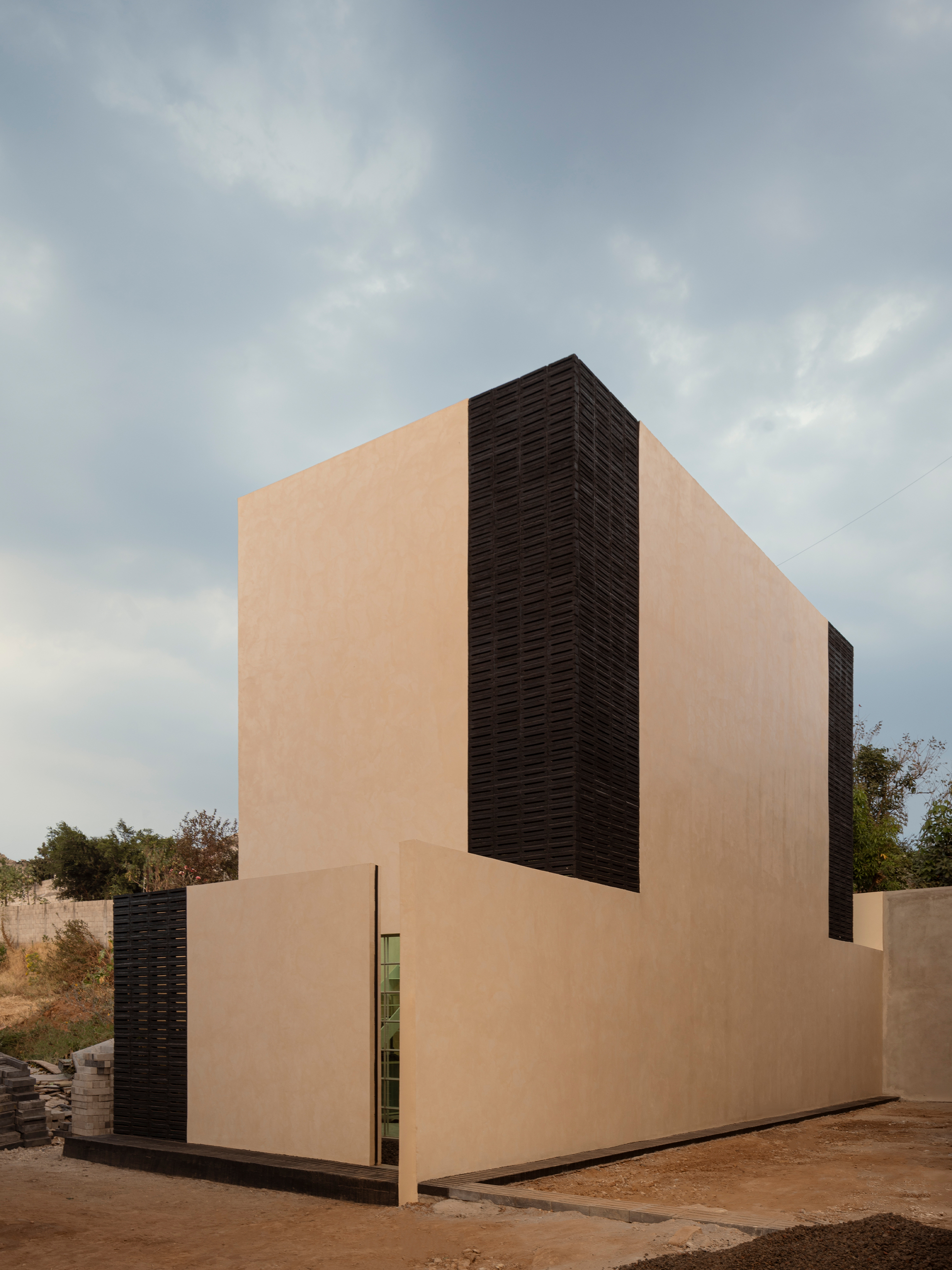 Two-story volume clad in smooth plaster and horizontal louvers under an overcast sky