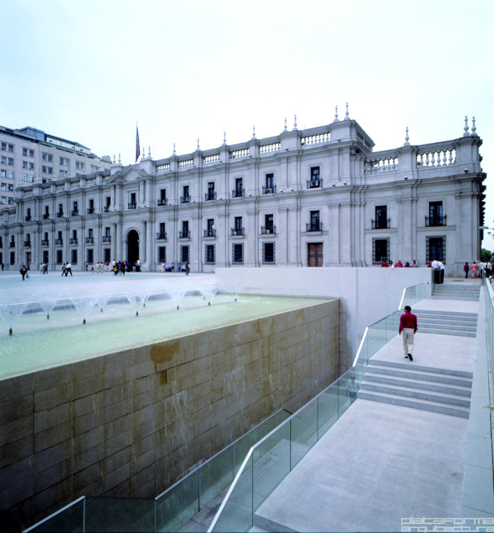 White marble stairs descending past a sandstone water feature wall toward the pale facade