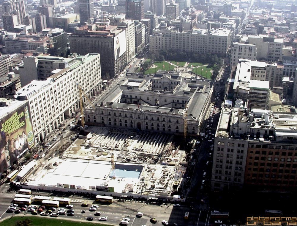 Aerial view showing construction excavation and white roofing in front of the historic palace block