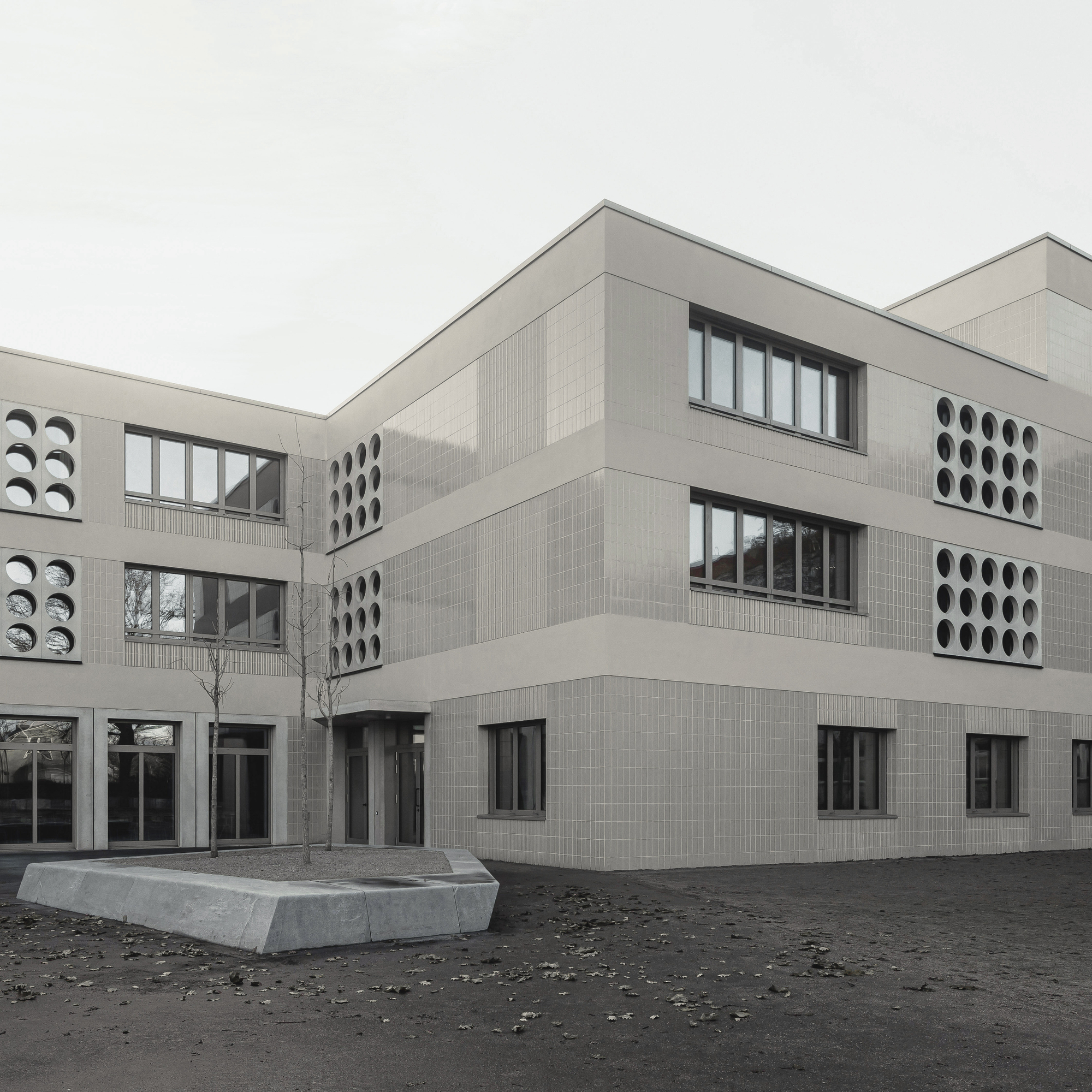 Corner view of the pale brick facade with circular perforated window panels and concrete planter in the courtyard