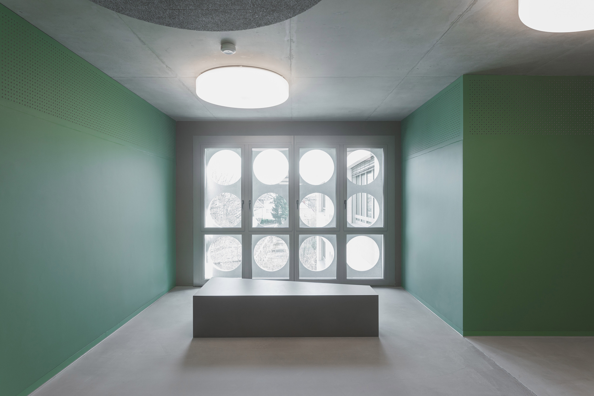 Interior room with green perforated wall panels and grid of circular windows beneath drum pendant lights