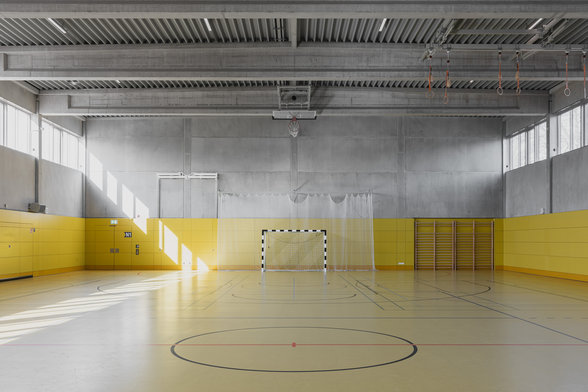 Gymnasium with yellow wall padding and exposed steel ceiling beams with sunlight streaming through high windows