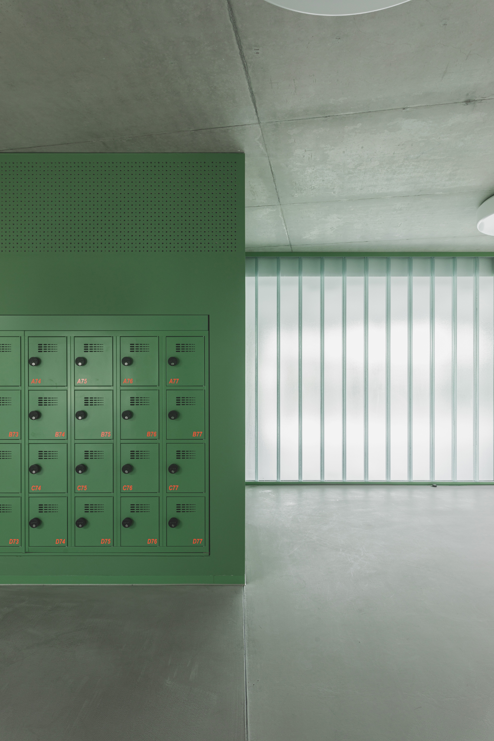 Interior hallway with green metal locker bank, exposed concrete ceiling, and vertical translucent wall panels