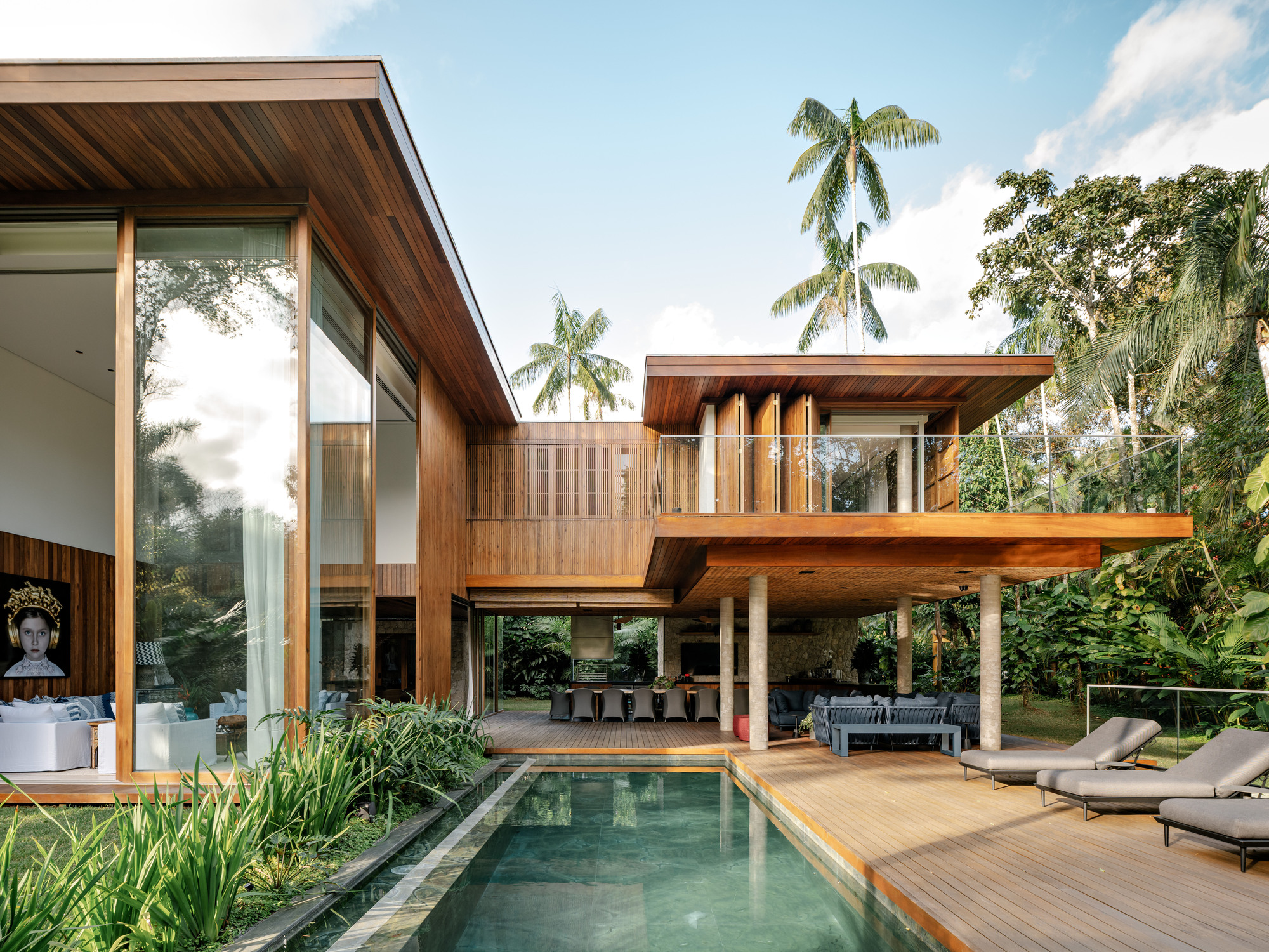 Garden view of the timber-clad volumes with open terrace, pool deck and palm trees