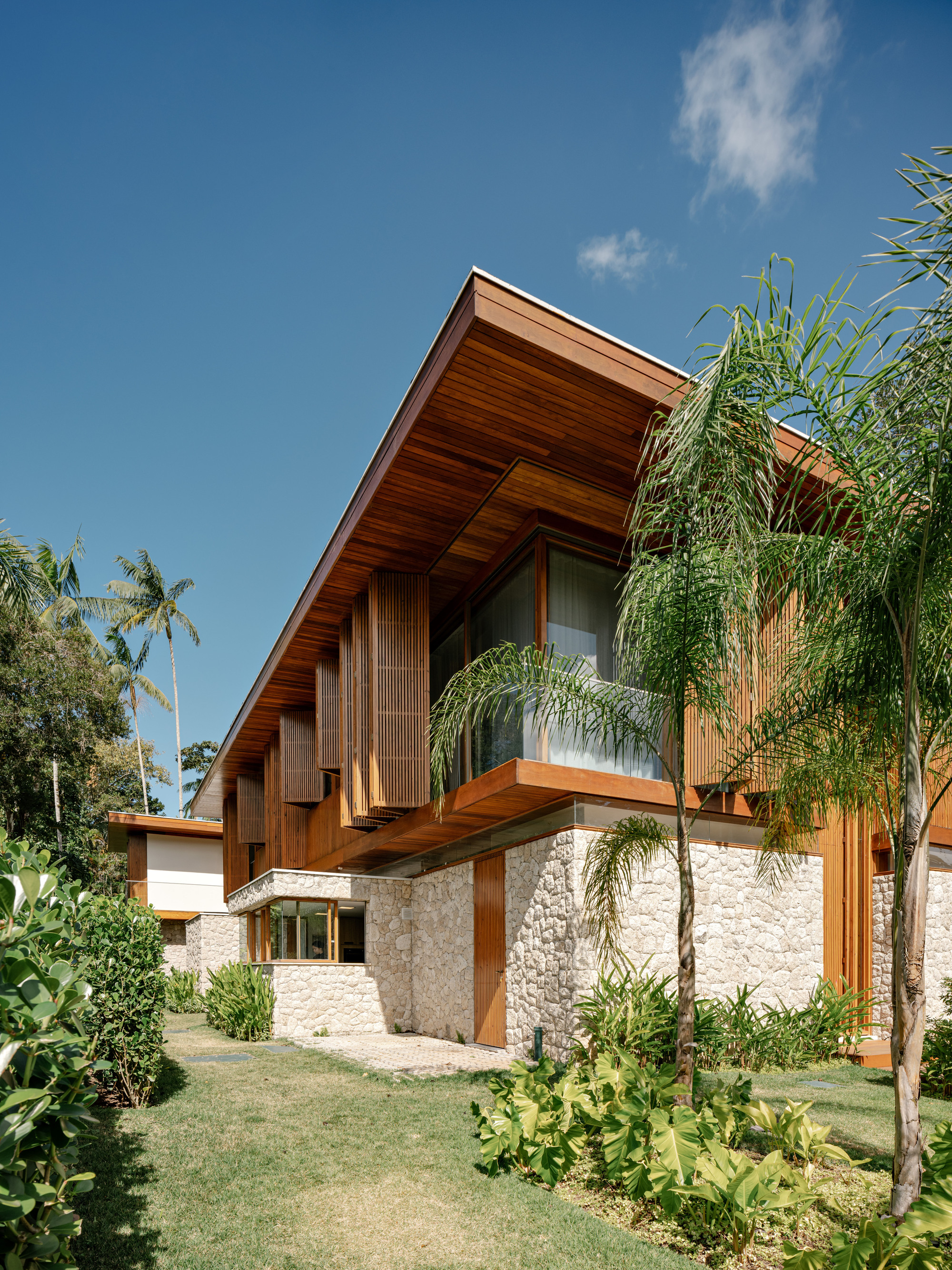 Street facade showing cantilevered timber box above stone base wall with vertical wood slats