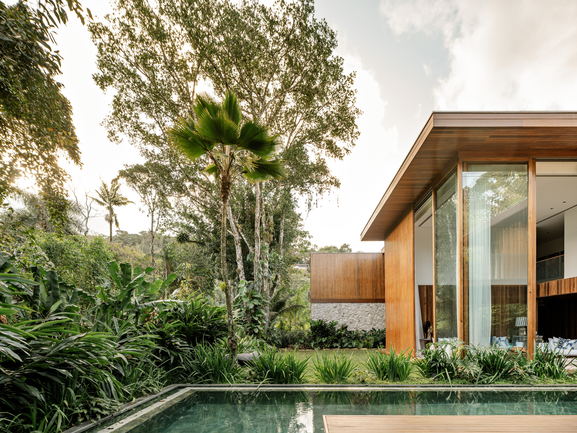 Pool edge with timber pavilion and floor-to-ceiling glazing framed by tropical planting