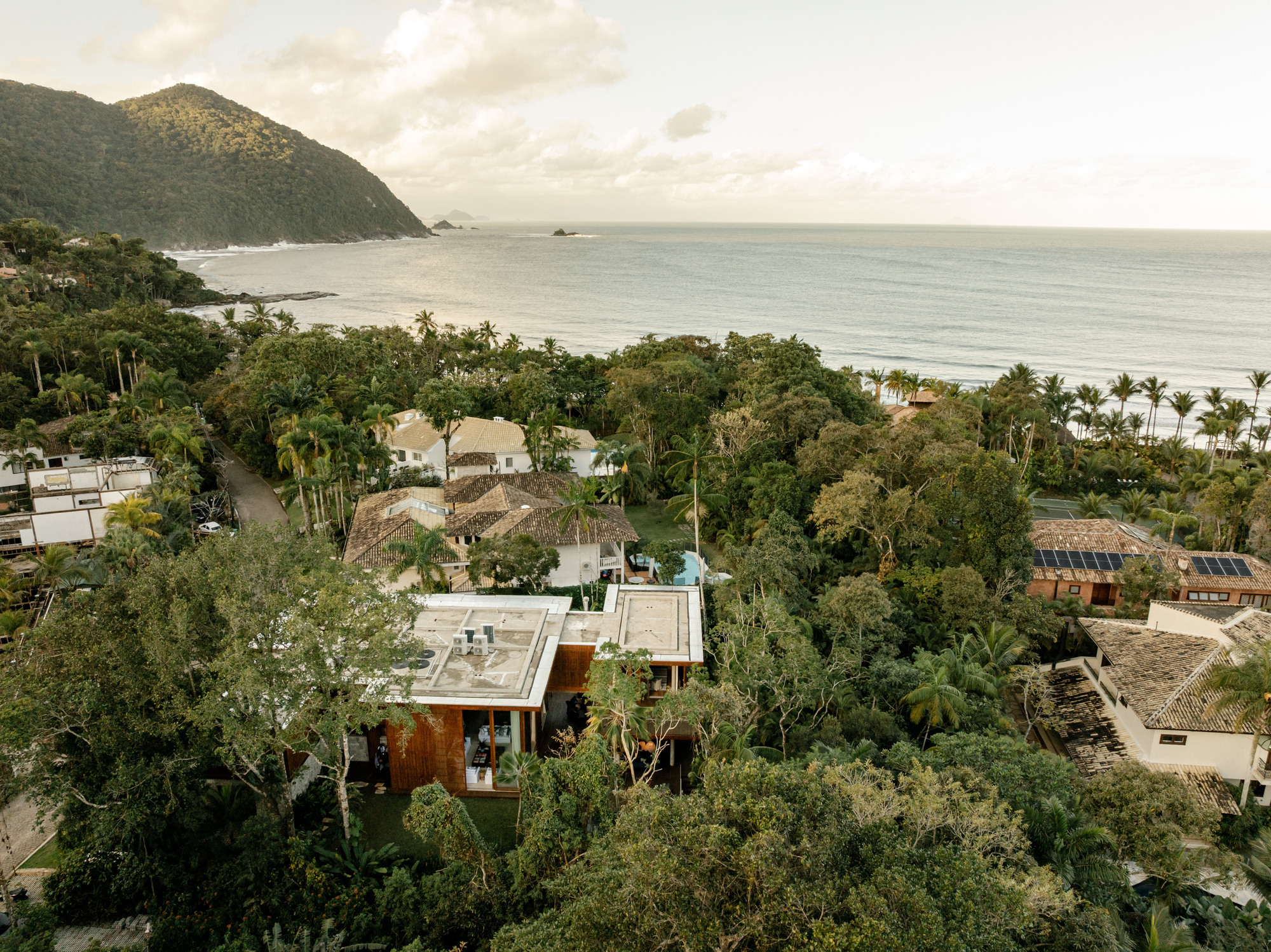 Aerial view of the house nestled in coastal vegetation between forested hillside and beach
