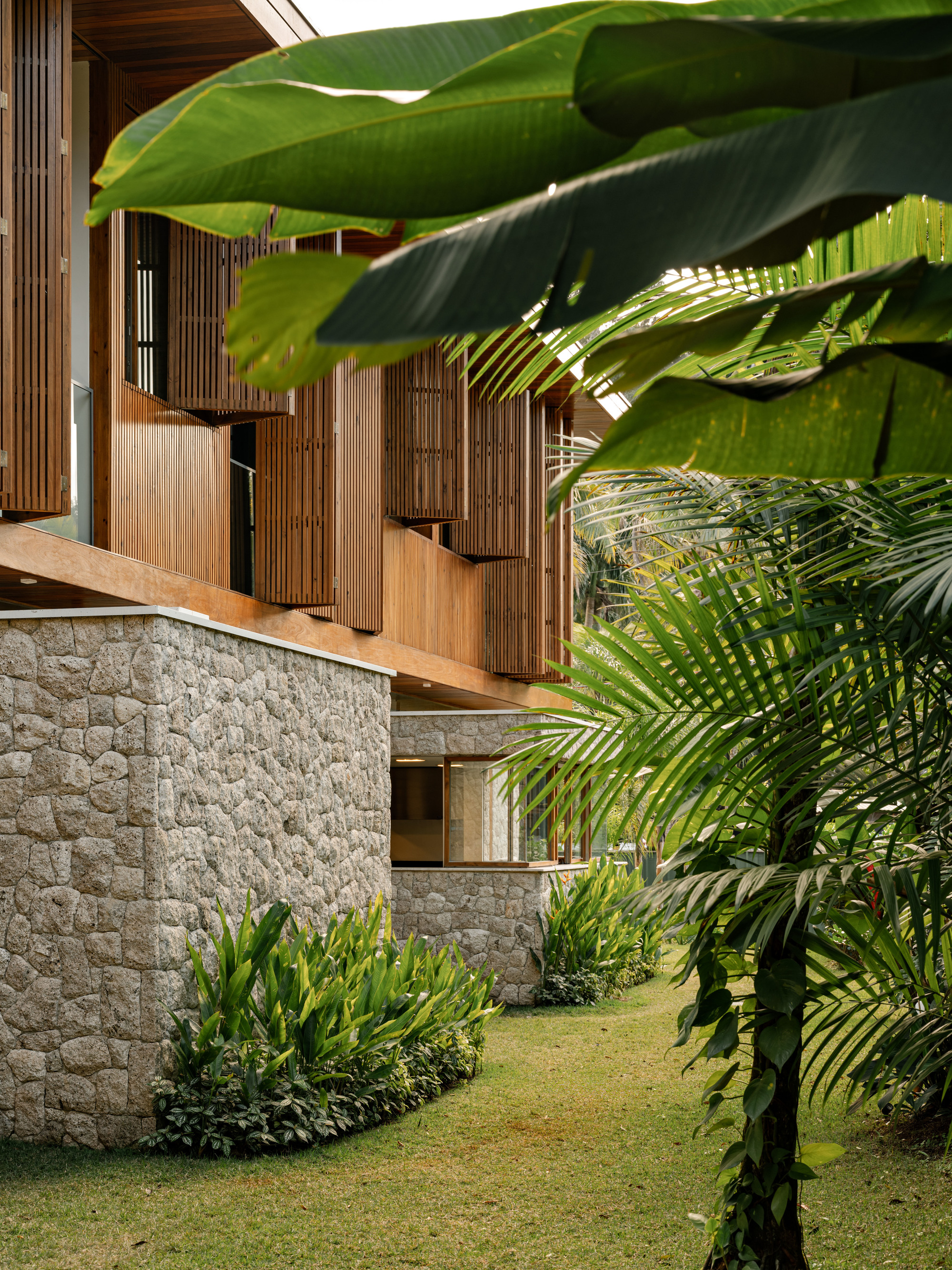 Exterior staircase with vertical timber screens and stone base wall framed by banana leaves