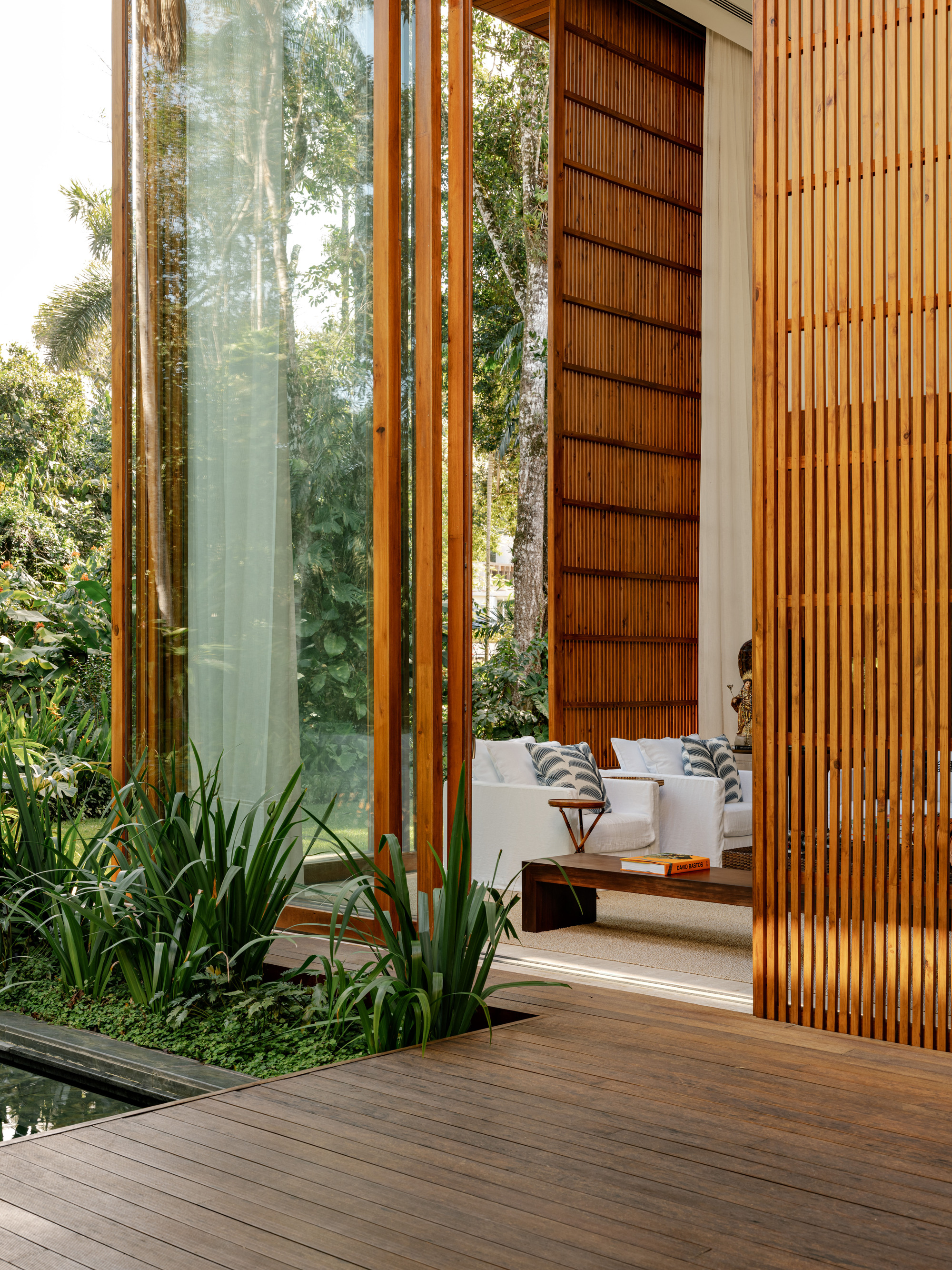 Covered timber deck with sliding louvered panels and vertical screen beside planted bed