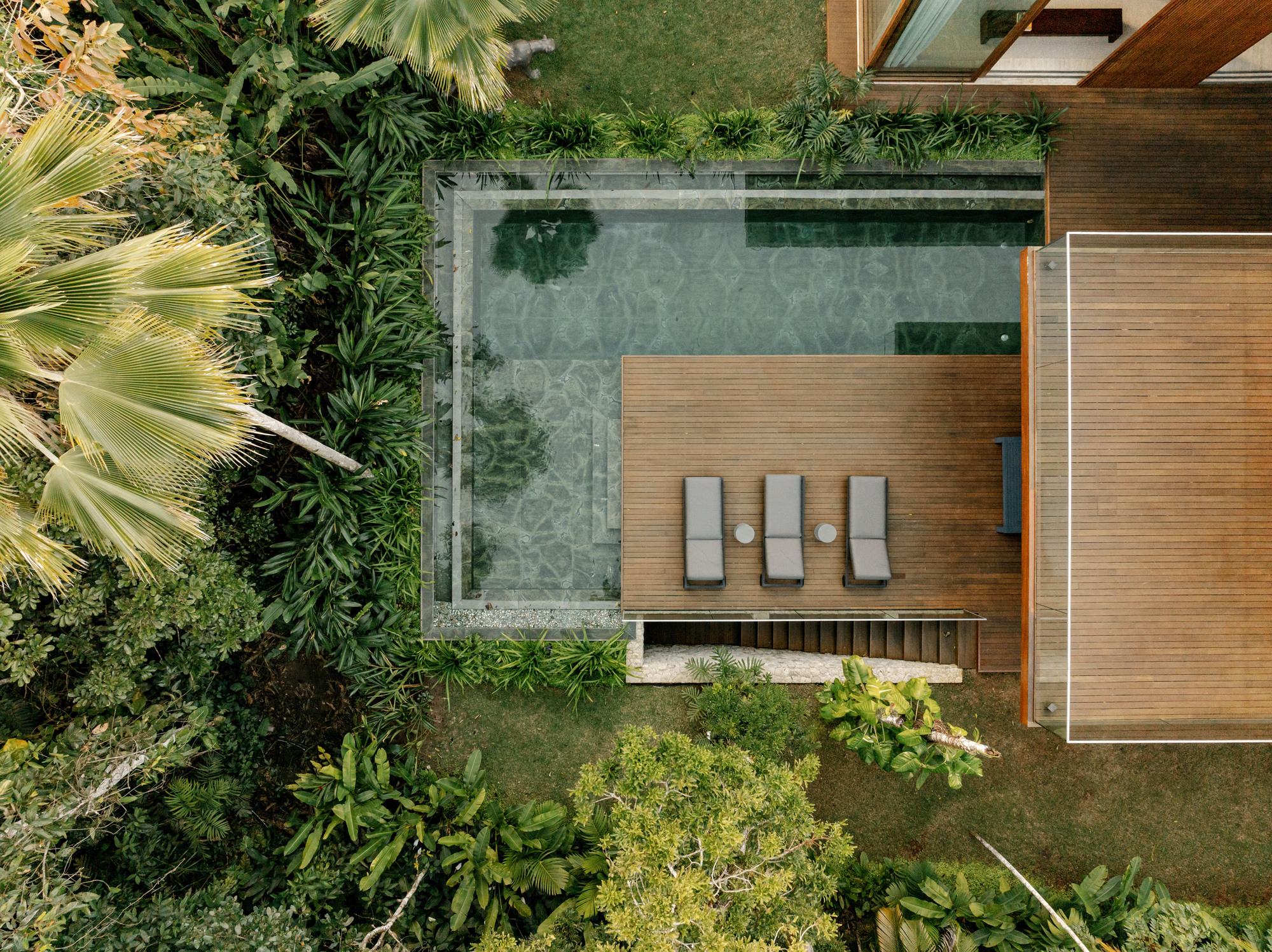 Aerial view of the timber deck, stone-edged pool, and three lounge chairs surrounded by tropical planting