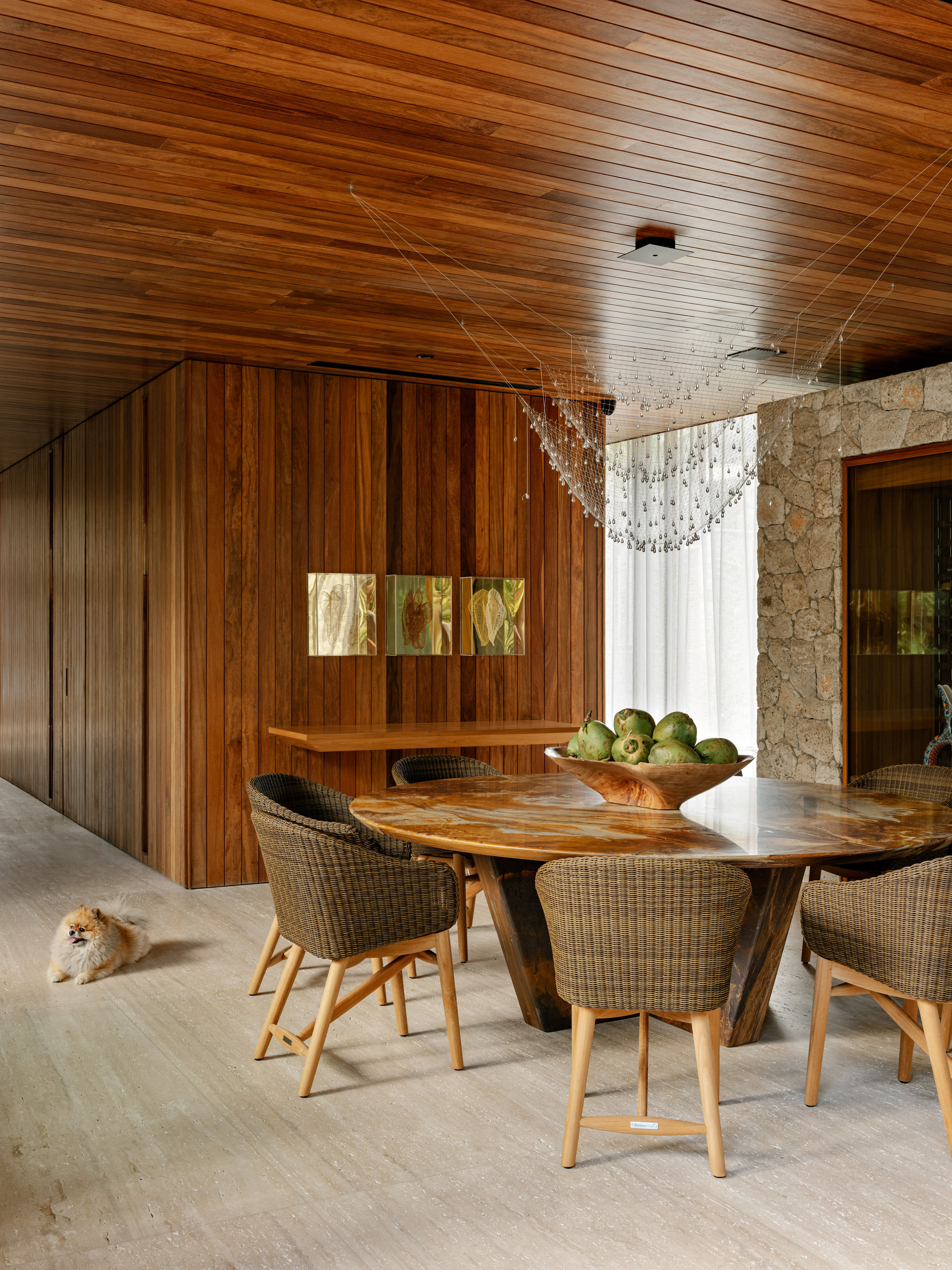 Dining area with timber slat ceiling, stone wall, and sculptural chandelier above a live-edge table
