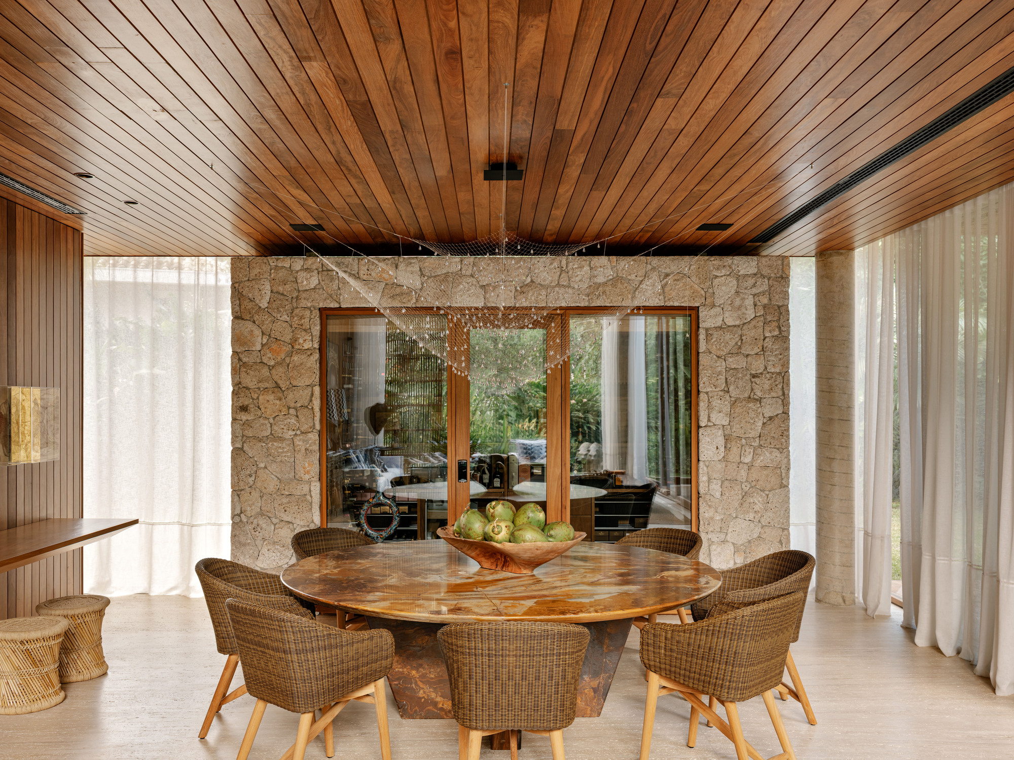 View of the dining table through timber-framed openings in the stone wall under a slatted ceiling