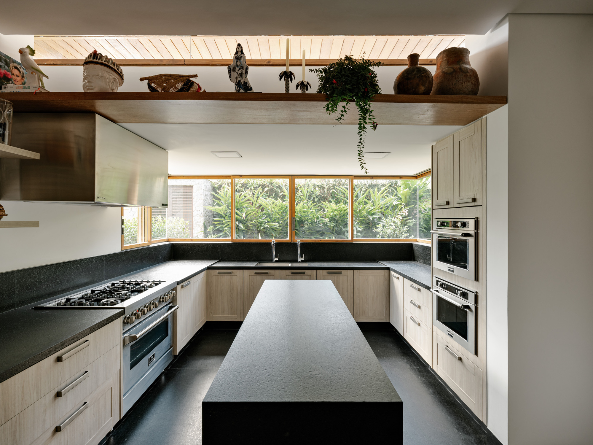 U-shaped kitchen with black stone countertops, timber cabinetry, and ribbon windows overlooking greenery