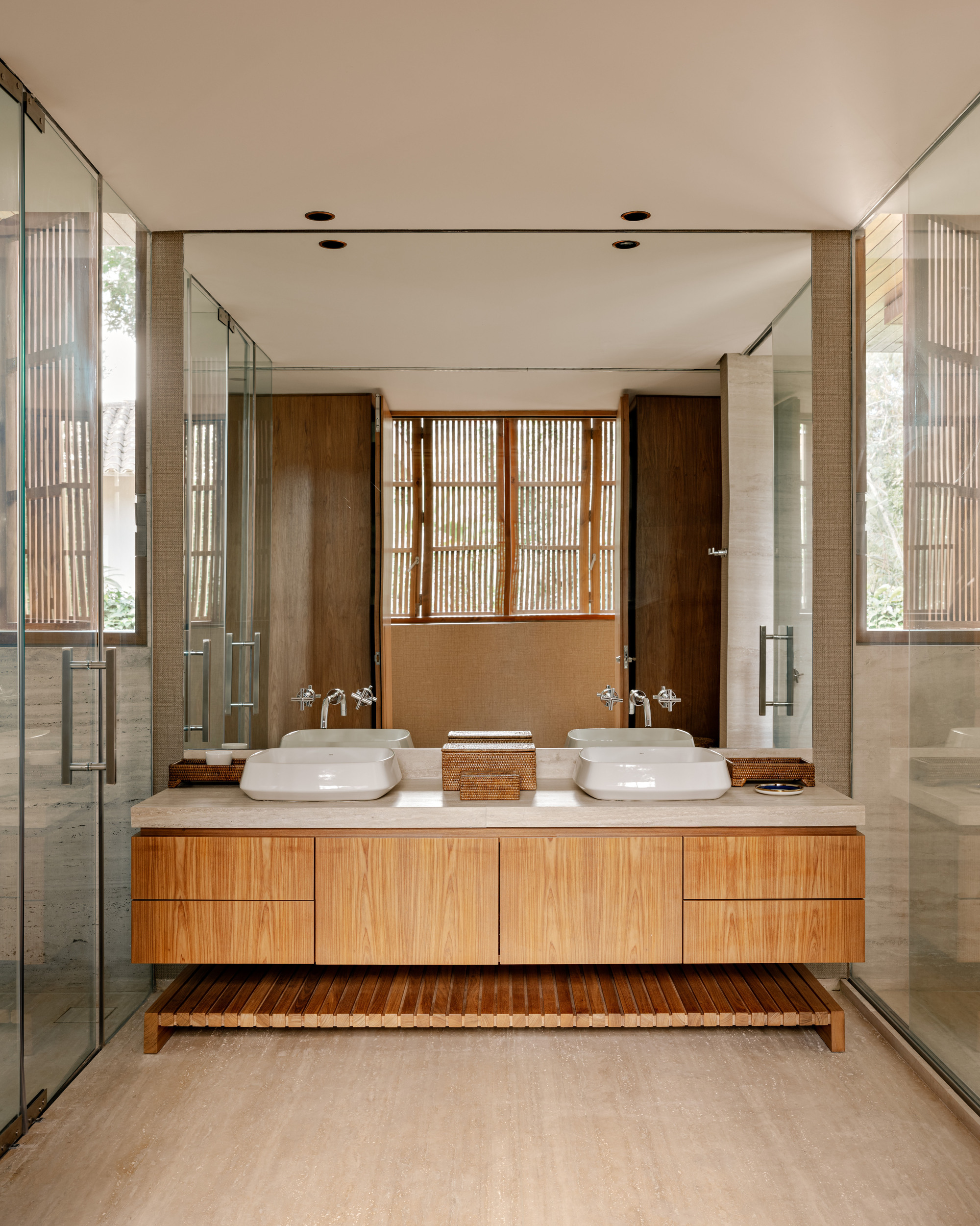 Bathroom vanity with twin vessel sinks on floating timber cabinet flanked by glass partitions
