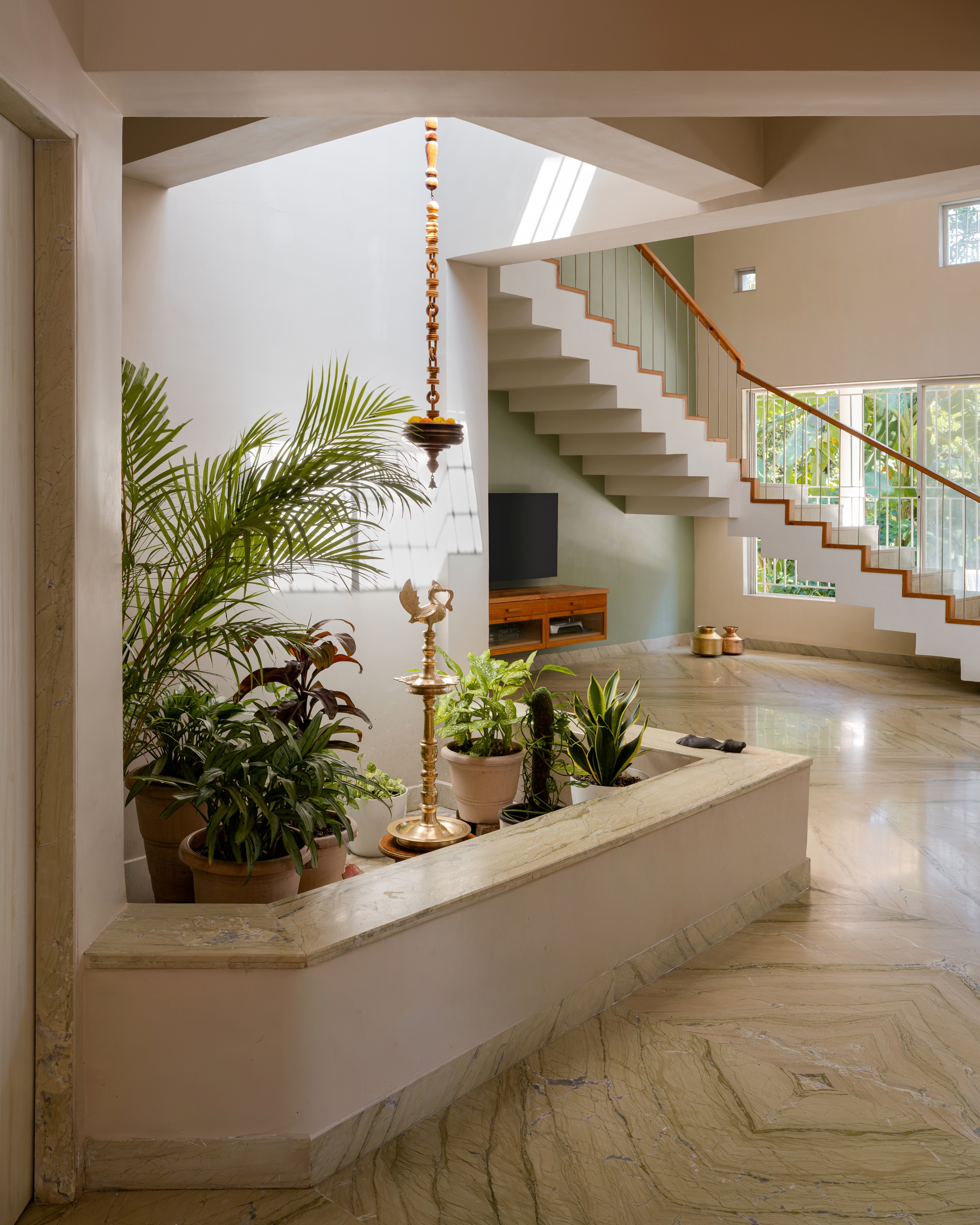 Entry foyer with floating staircase, vertical metal balustrade, and potted plants beneath a suspended brass lamp
