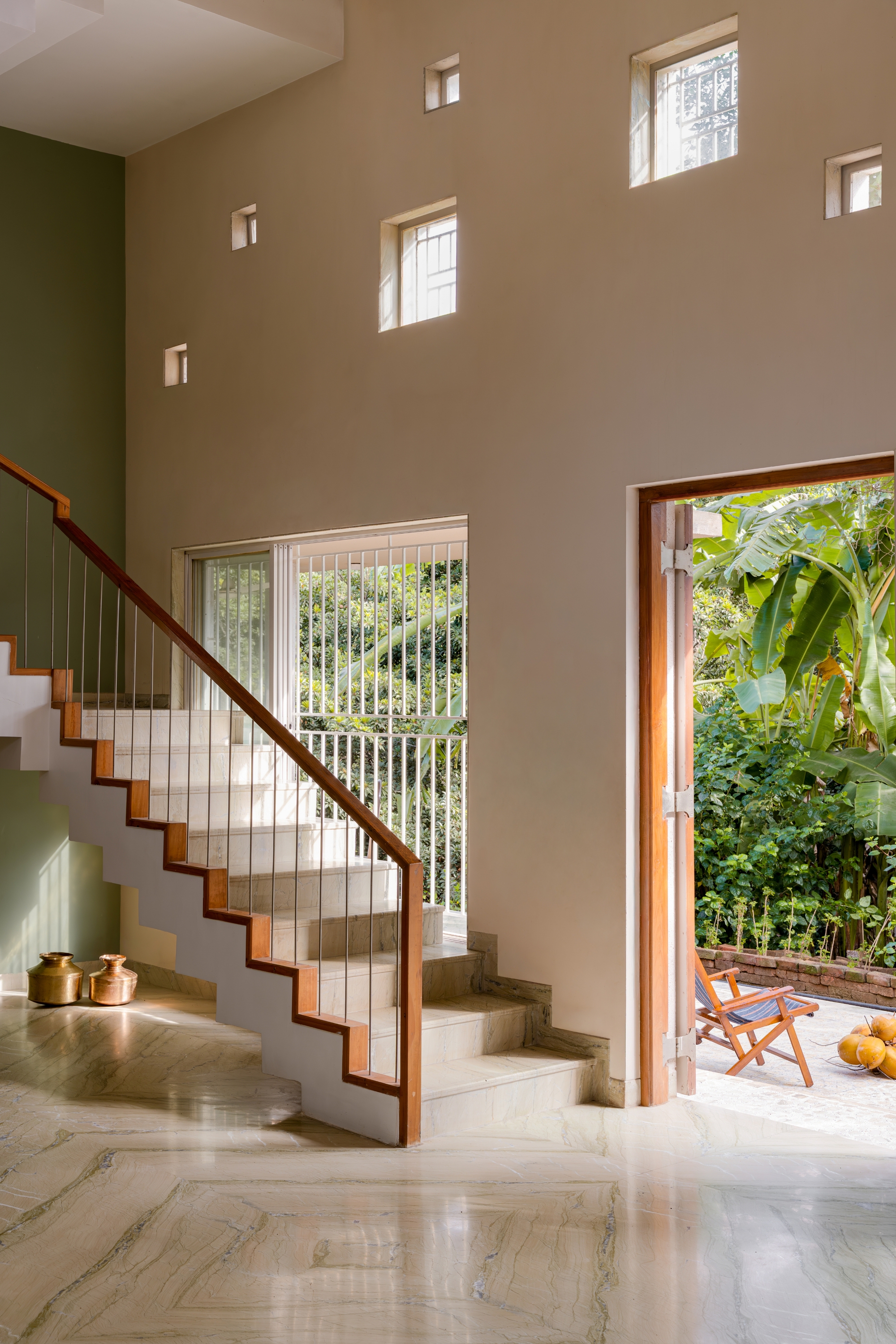 Double-height stairwell with polished stone treads, vertical railings, and scattered square windows framing greenery outside