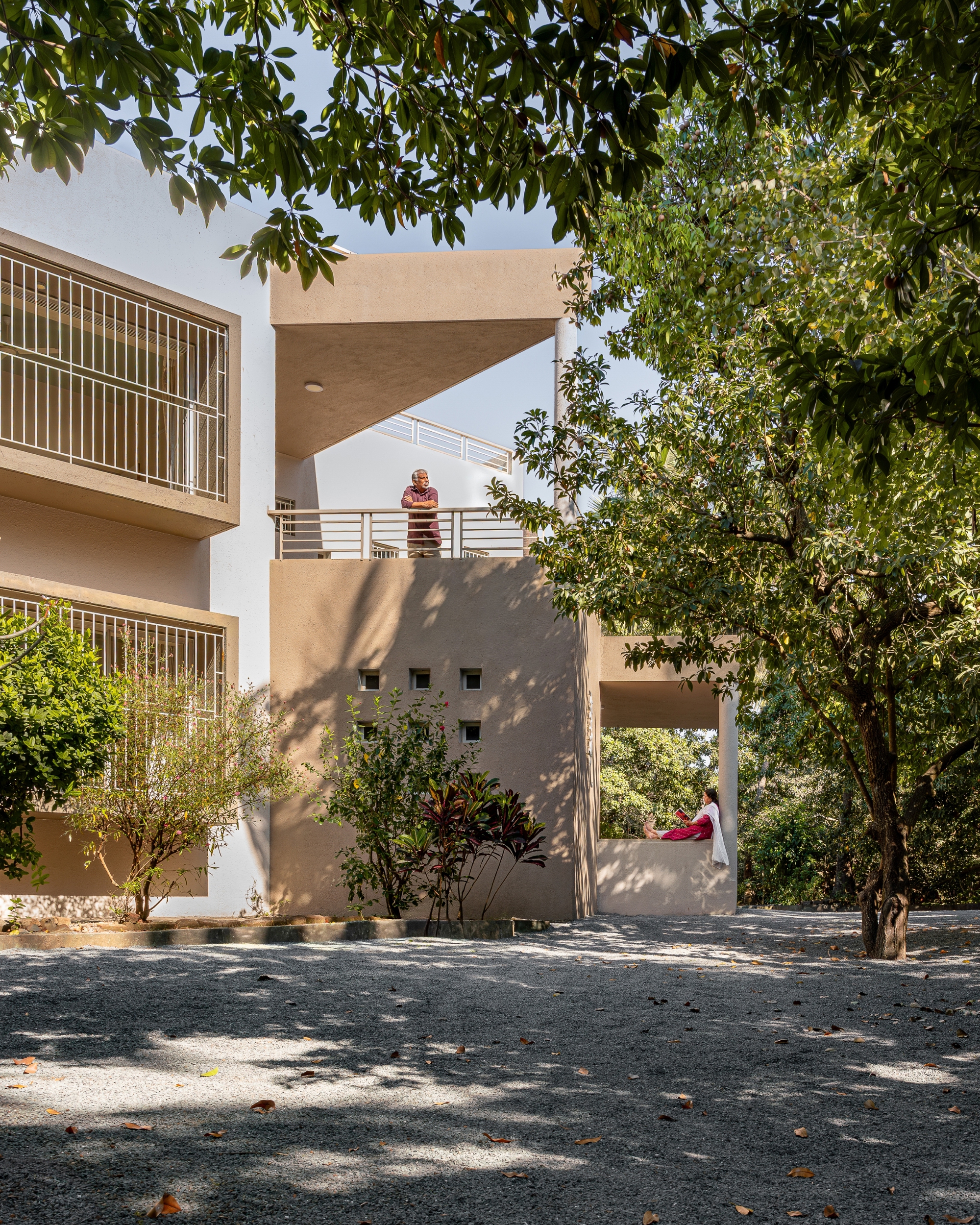 Courtyard facade with cantilevered canopy, metal railings and dappled tree shadows on gravel surface