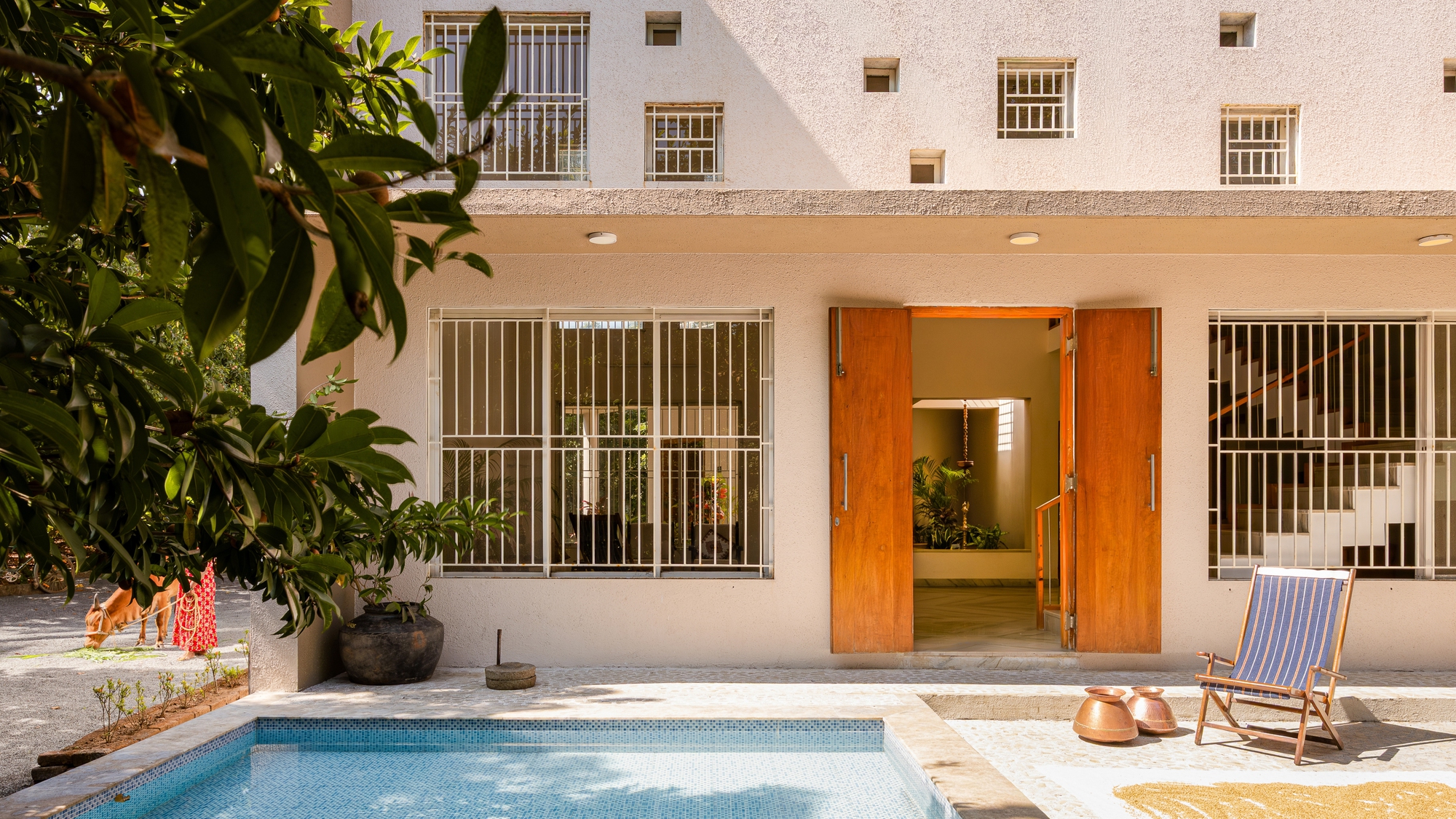Rear facade with timber pivot doors, metal window grilles and raised pool at dusk