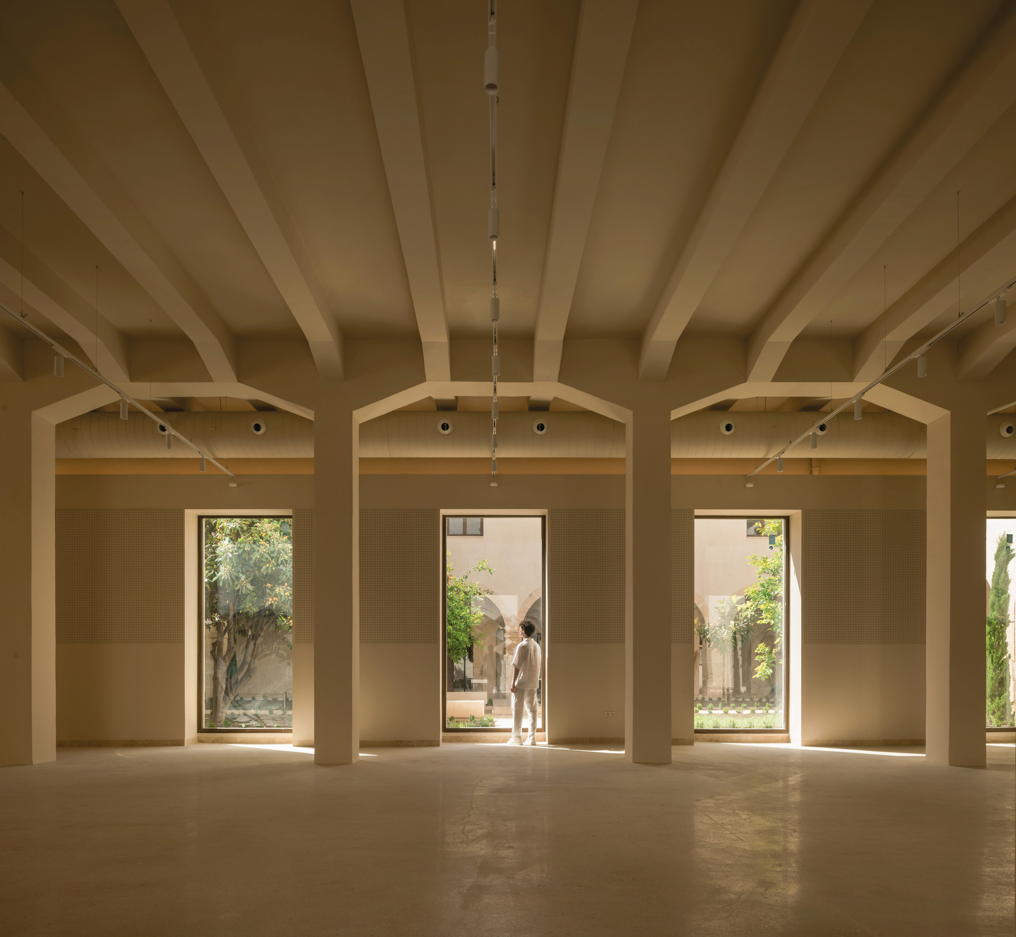 Interior gallery with exposed timber beams, arched openings, and a figure standing in the central doorway