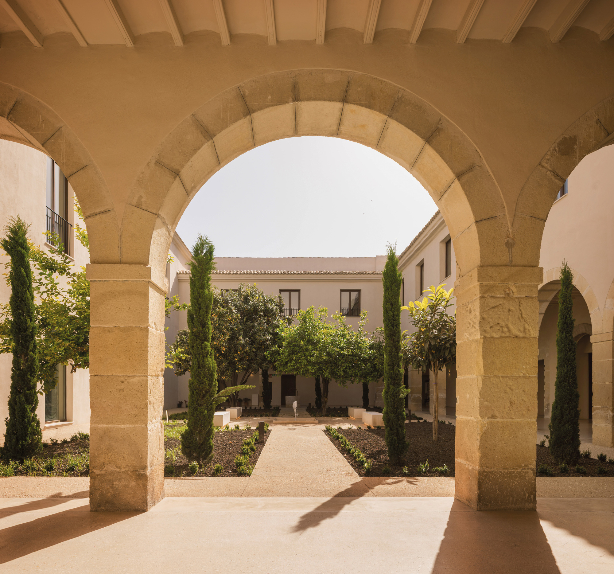 View through the stone voussoir arch framing the courtyard garden with cypresses and gravel paths
