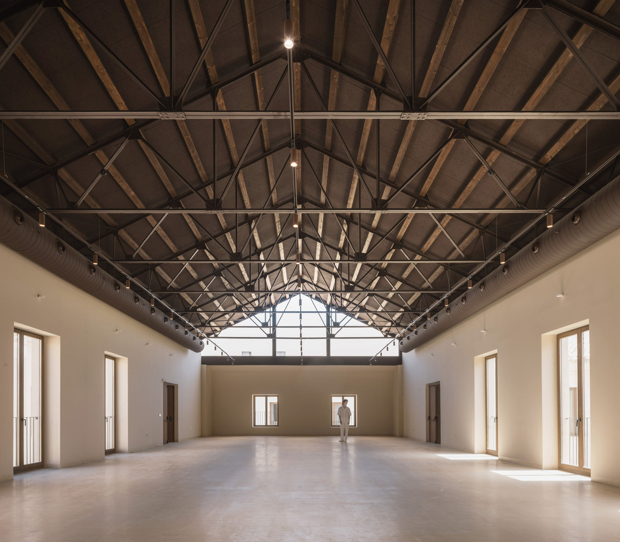 Interior hall with exposed timber truss roof structure and a single figure standing in the central bay