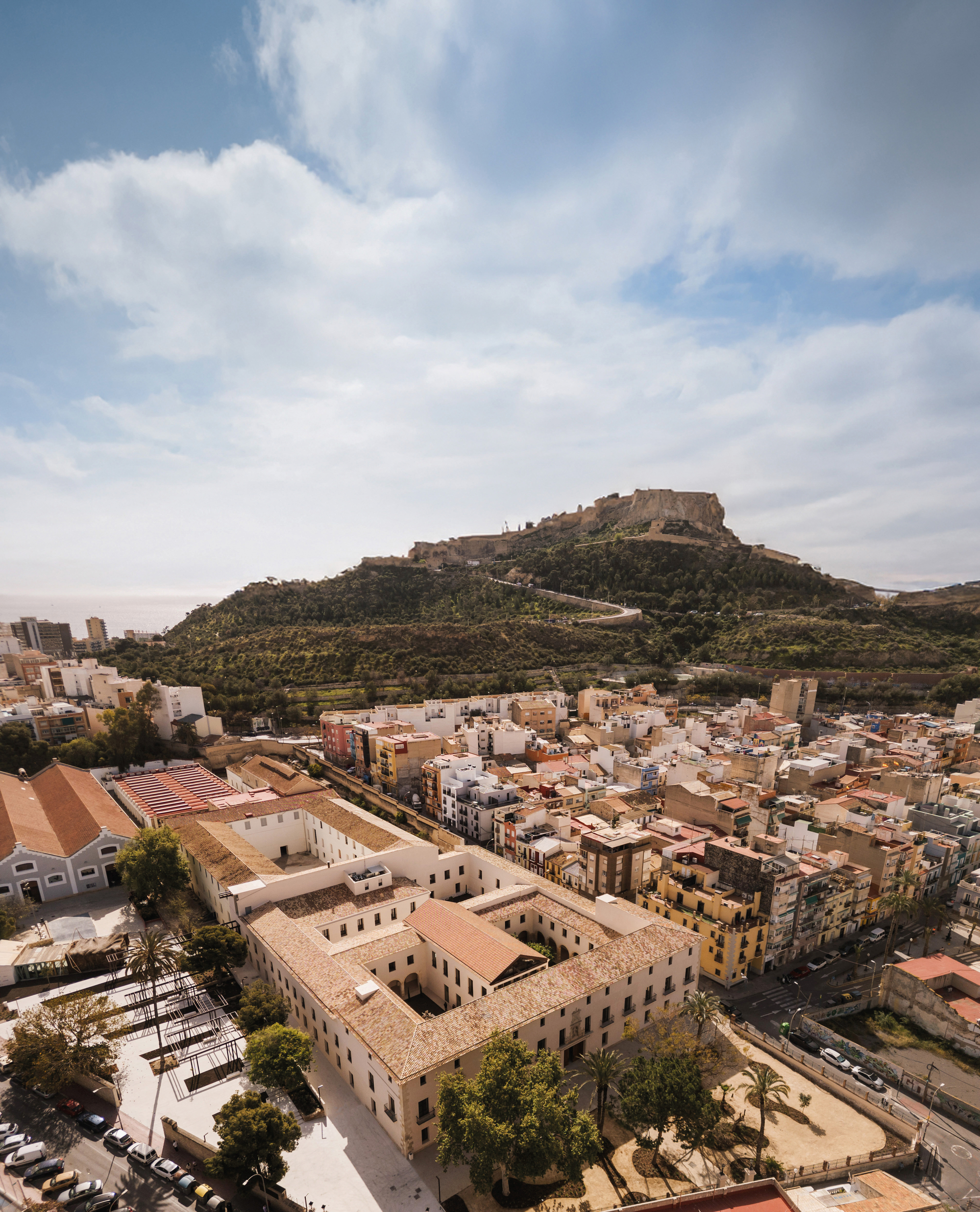Aerial view of the quadrangular courtyard complex set within a hillside town below afternoon clouds