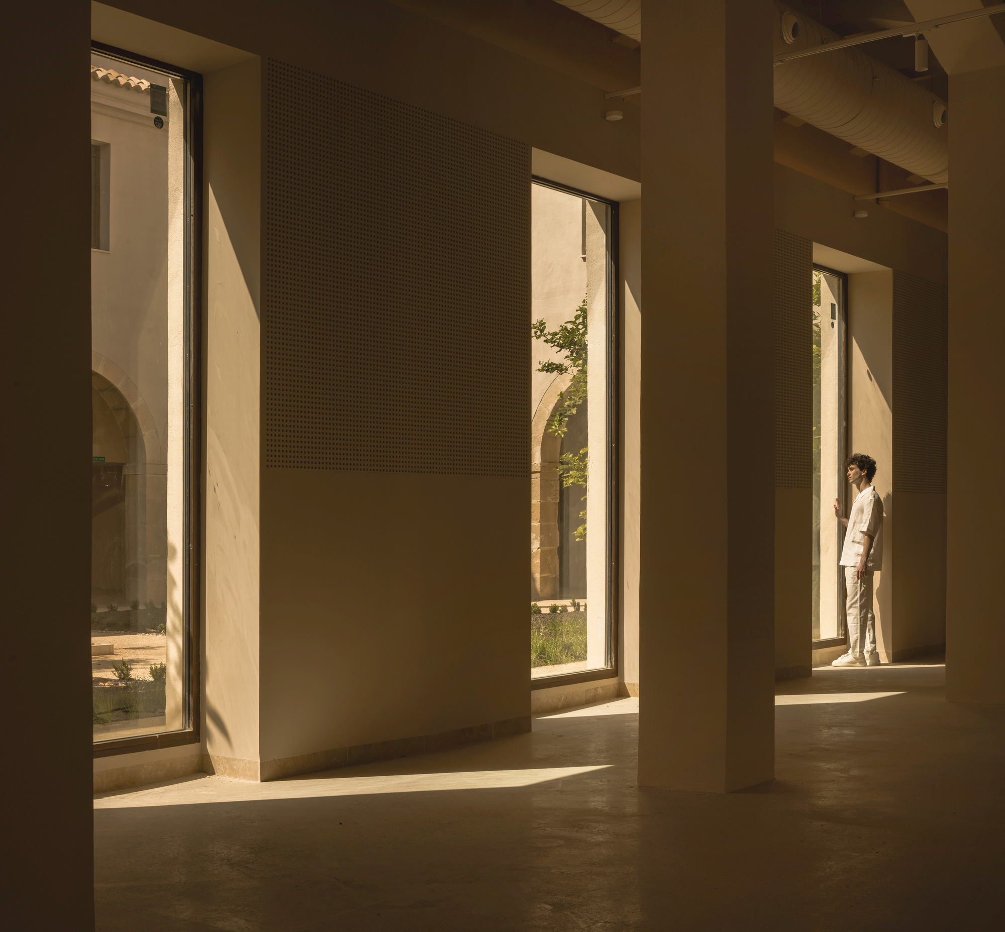 Sequence of tall openings with perforated panel walls and a figure in warm afternoon light