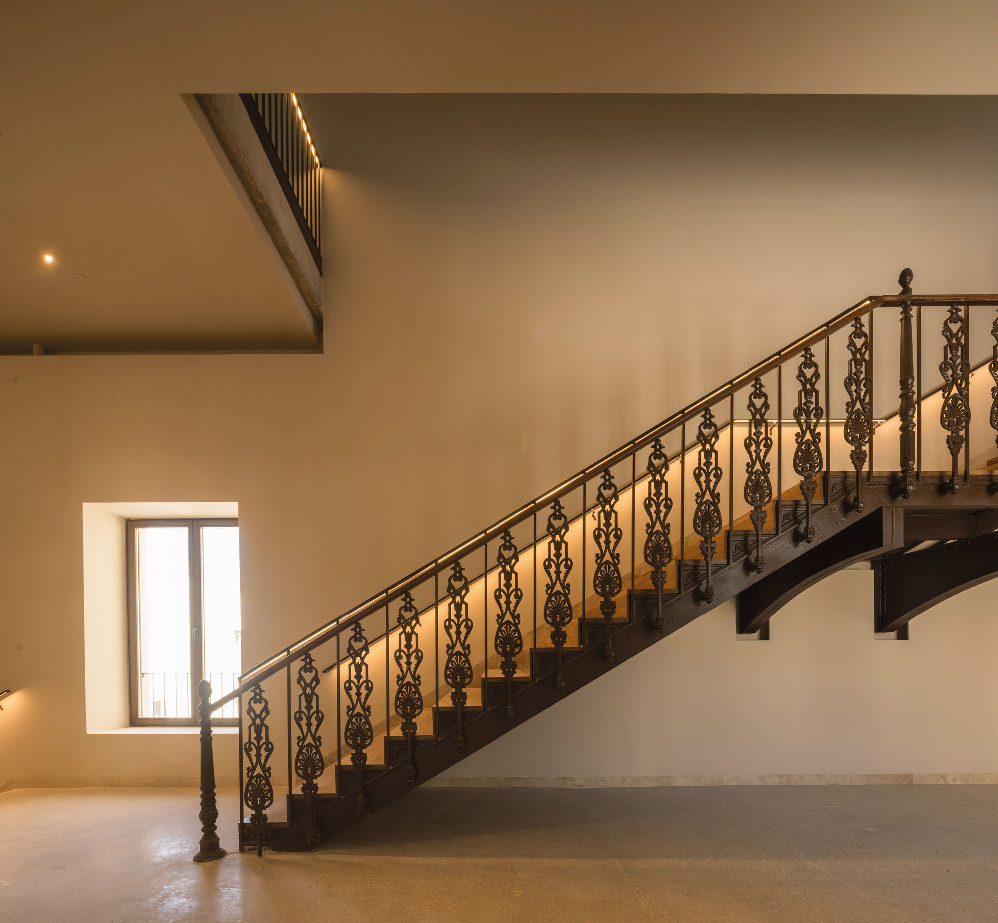 Staircase with ornamental wrought iron balustrade rising to an upper level balcony at dusk