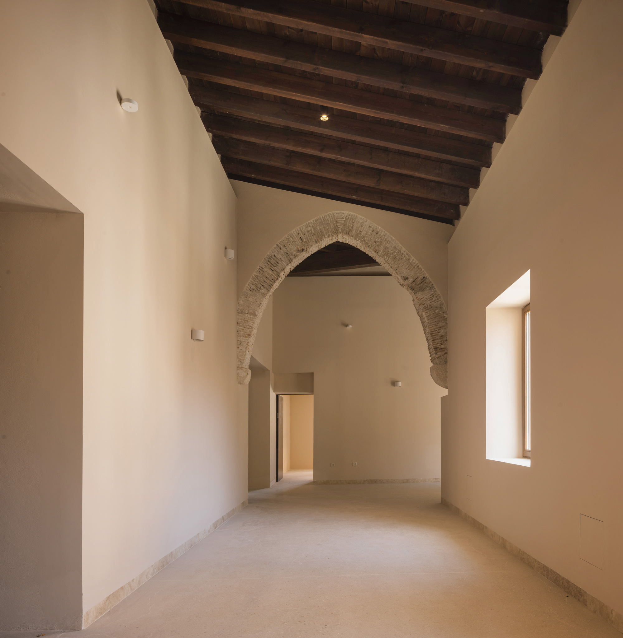 Interior corridor with exposed timber ceiling beams and brick archway framed by light plaster walls