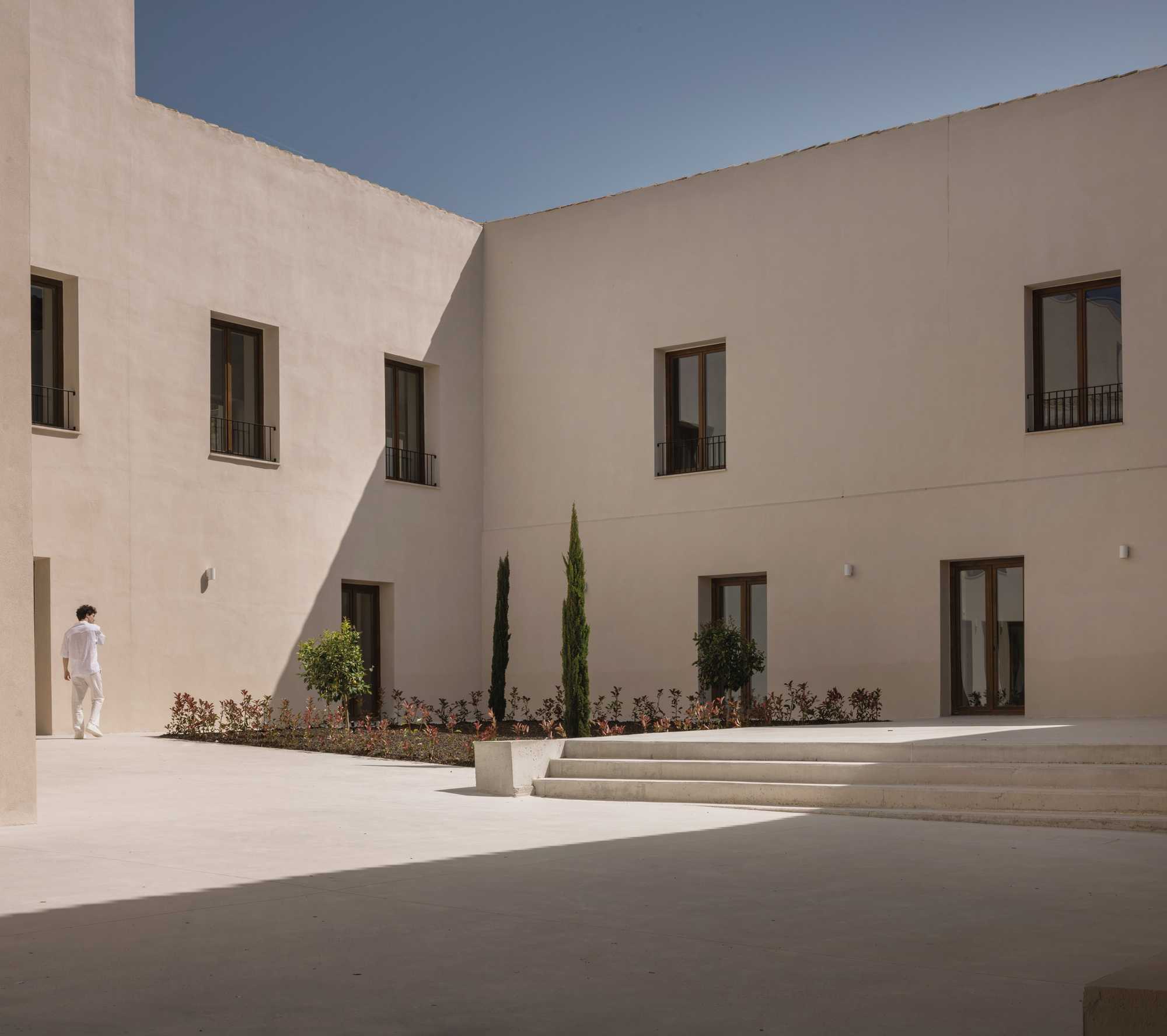 Interior courtyard with planted beds of cypress and shrubs as a person walks in sunlight