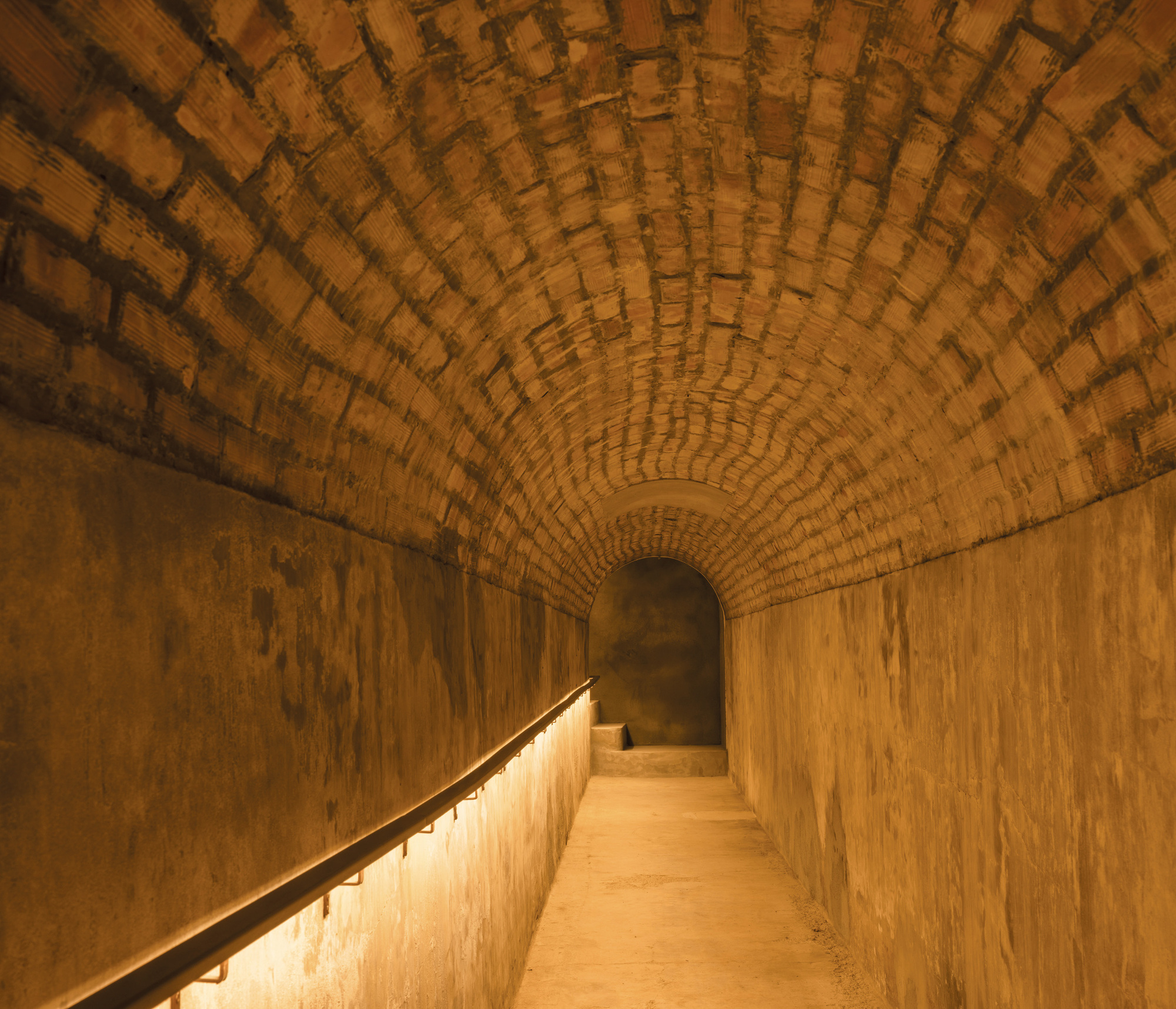 Vaulted brick corridor with integrated handrail lighting and receding arched ceiling pattern