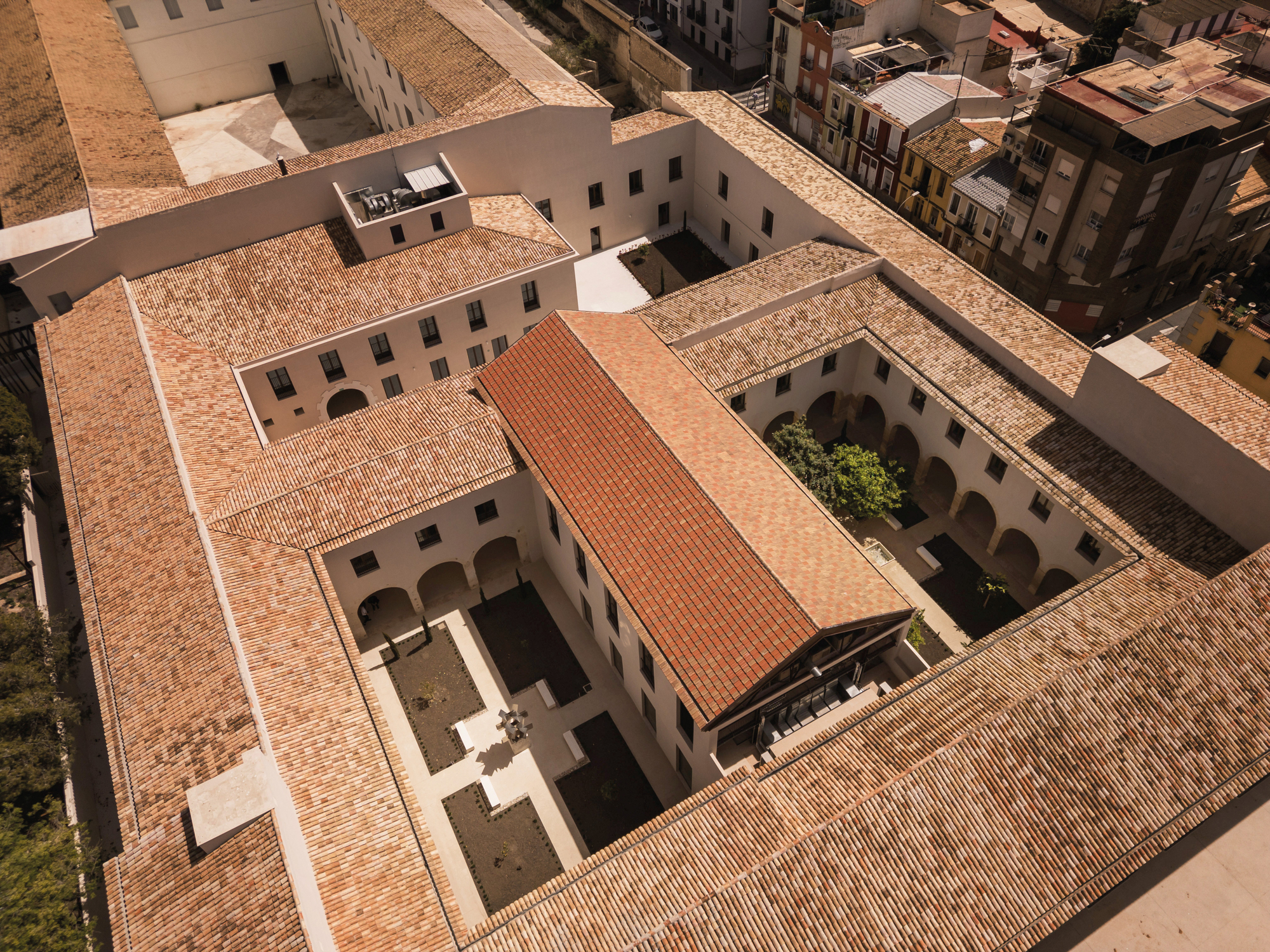Aerial view of the terracotta-tiled roofs arranged around two interior courtyards in bright sunlight