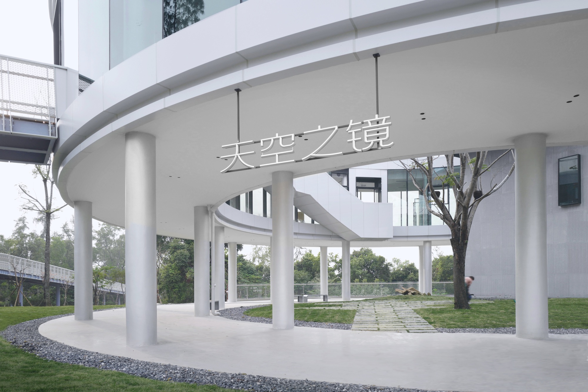 View beneath the elevated structure showing white cylindrical columns supporting the curved volume with signage overhead