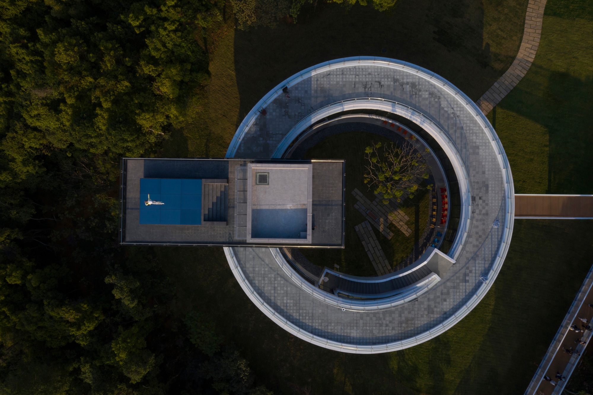 Top-down view of the double-ring structure with pool terrace and concentric tiled pathways amid green lawn