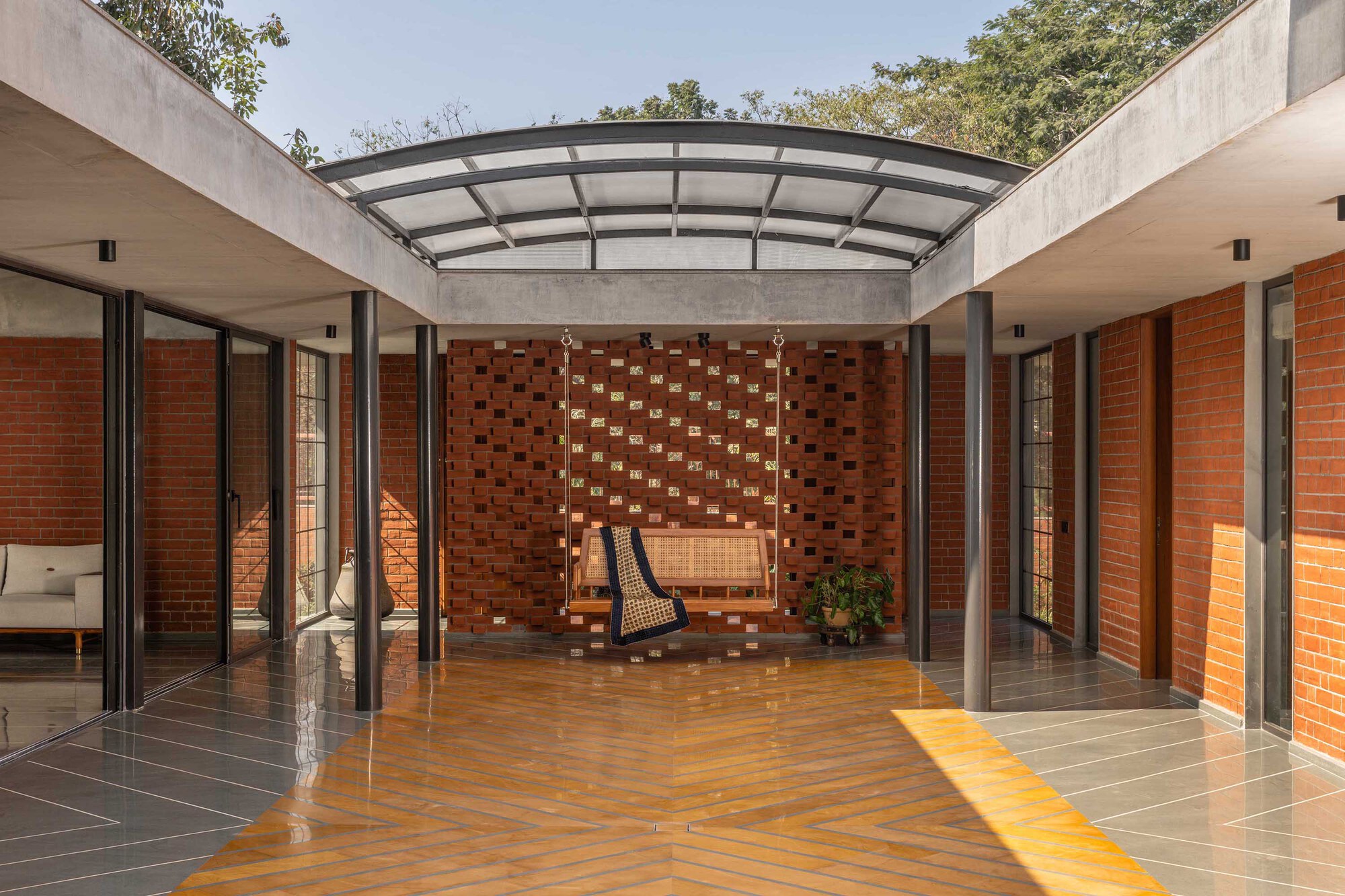 Central courtyard with perforated brick wall, concrete beams, and curved polycarbonate roof under dappled daylight