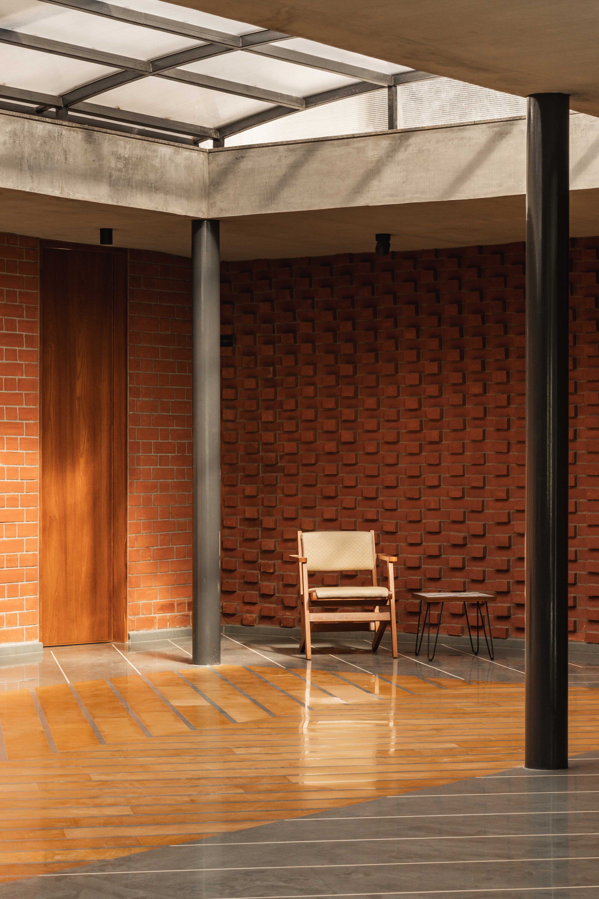 Slender steel columns supporting concrete beams and translucent roof panels above the terracotta-tiled courtyard floor