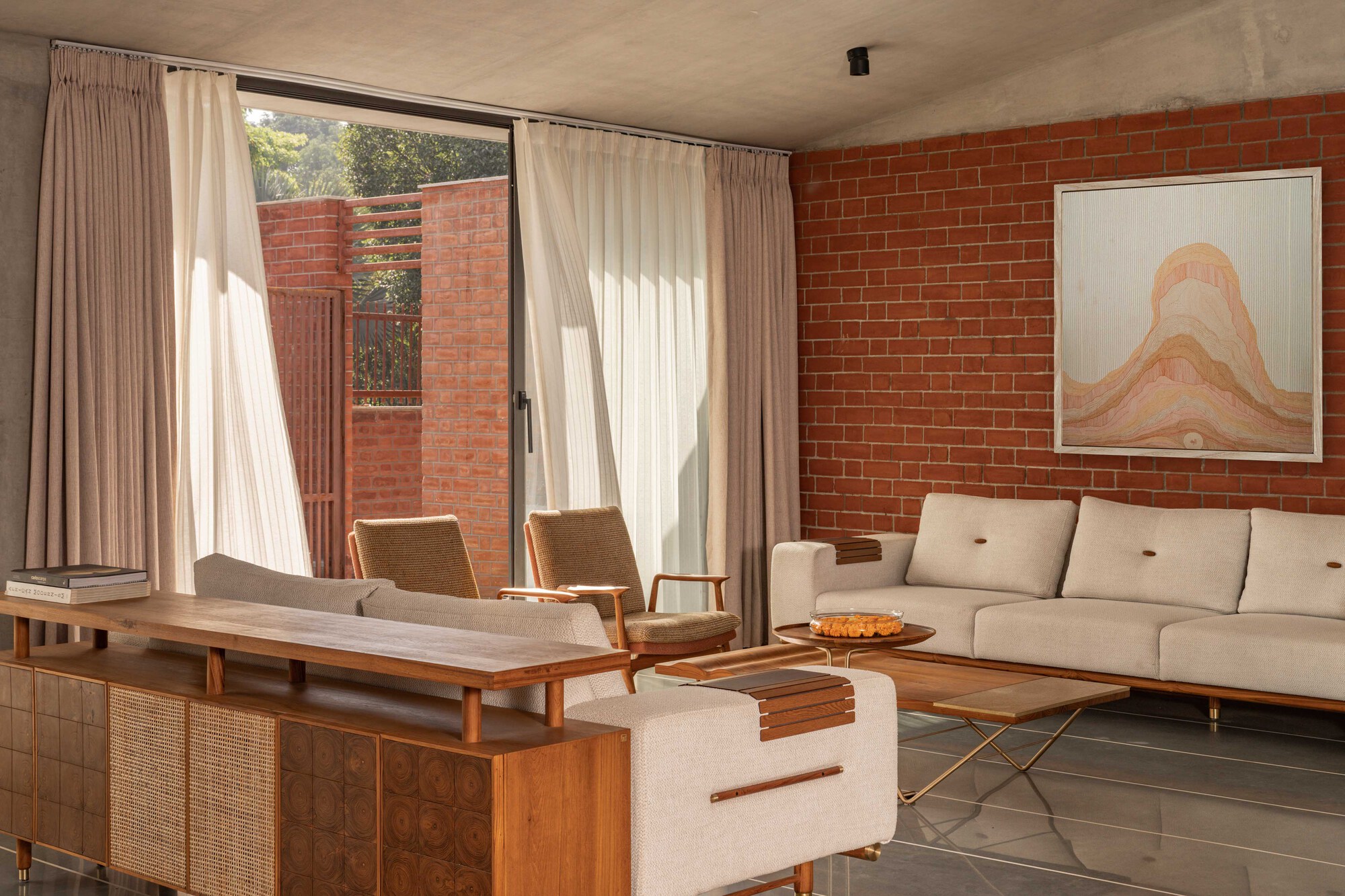 Living room with exposed brick walls, sheer curtains filtering afternoon light, and a view to the brick screen