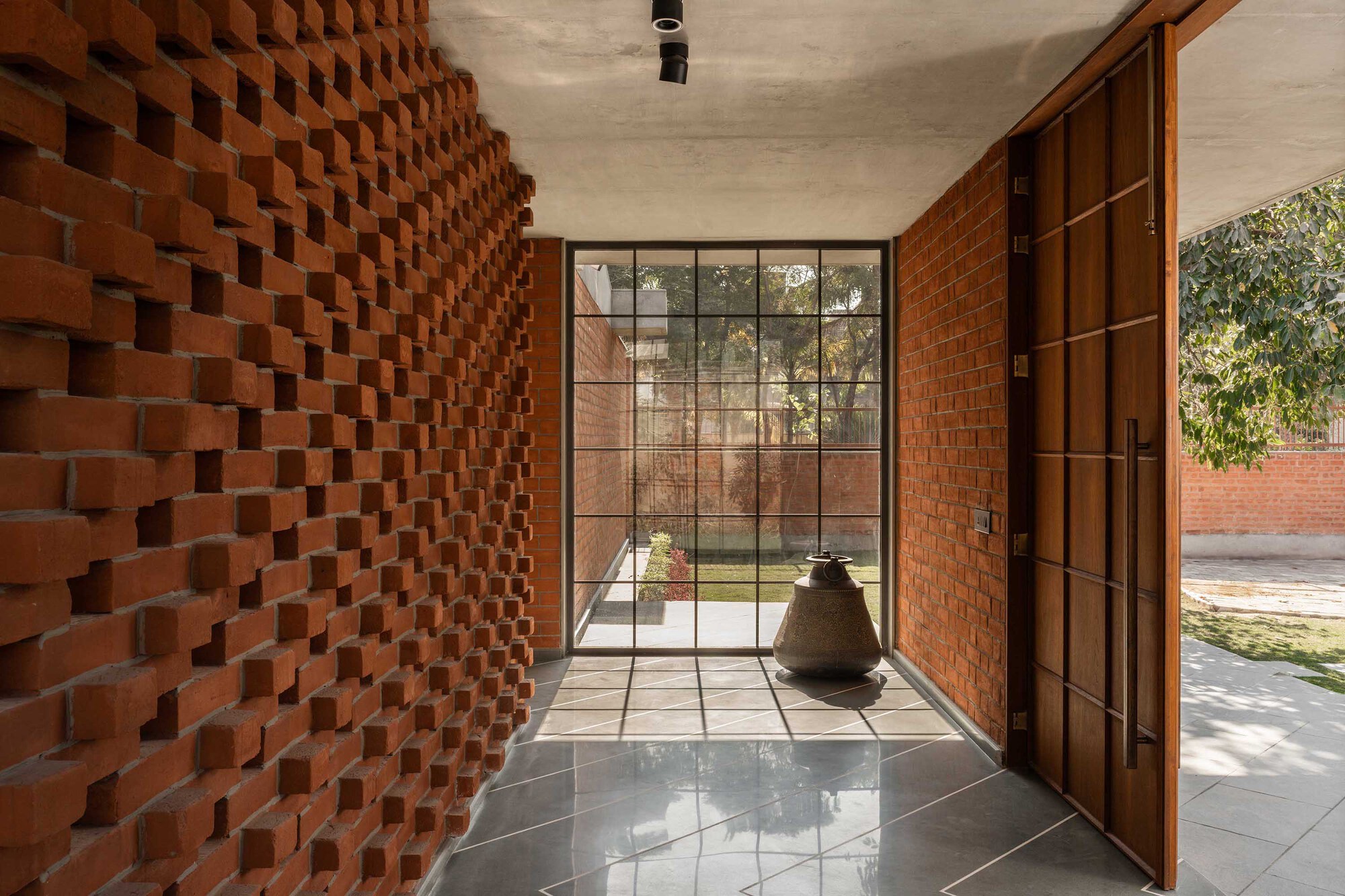 Entry vestibule with staggered brick wall, gridded steel-frame glazing, and concrete ceiling casting geometric shadows