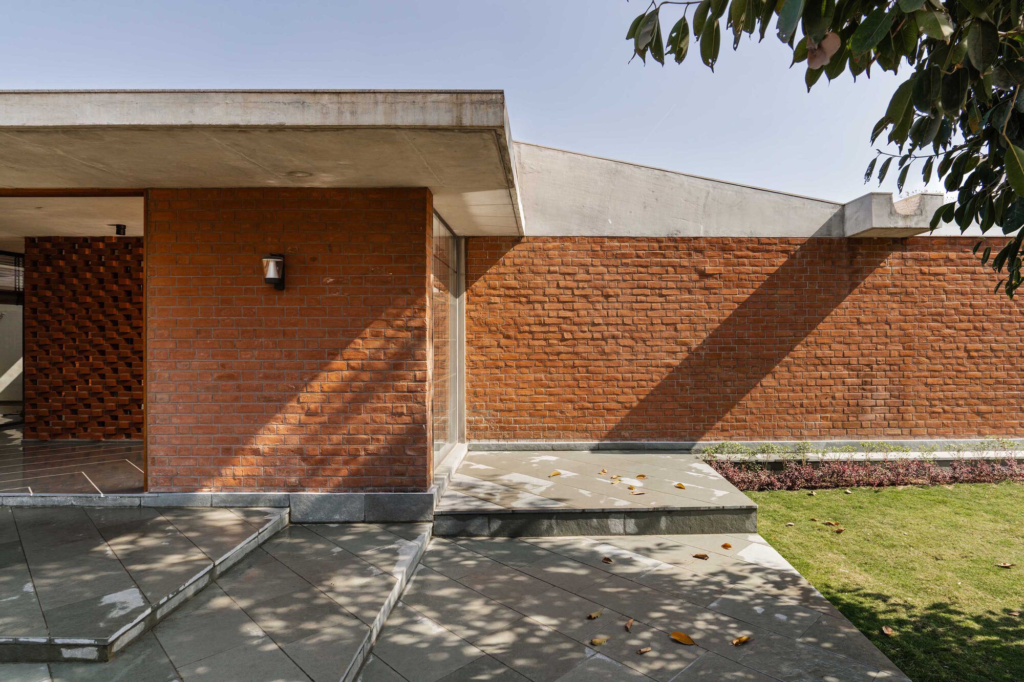 Patterned red brick courtyard wall with concrete canopy and dappled afternoon sunlight