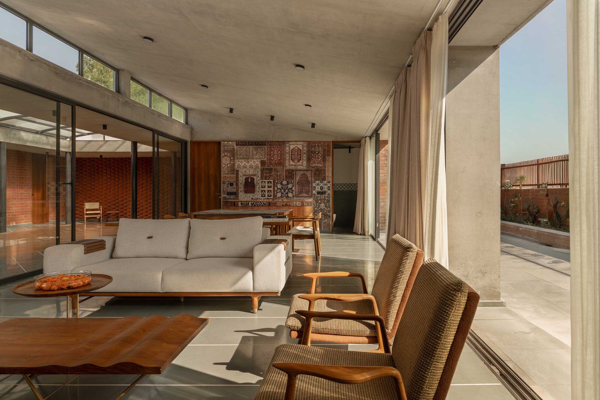 Living room with concrete ceiling, clerestory windows, and woven chairs facing a patterned textile wall