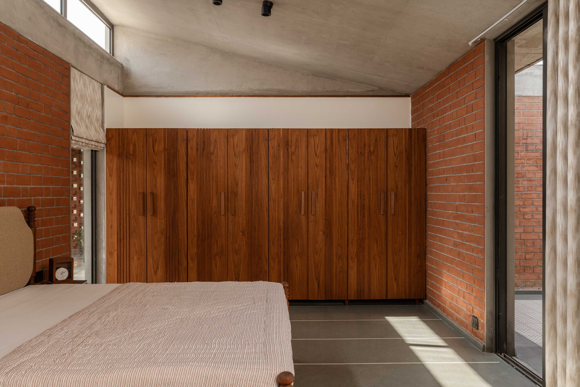 Bedroom with vertical timber wardrobe wall flanked by red brick and glass doors