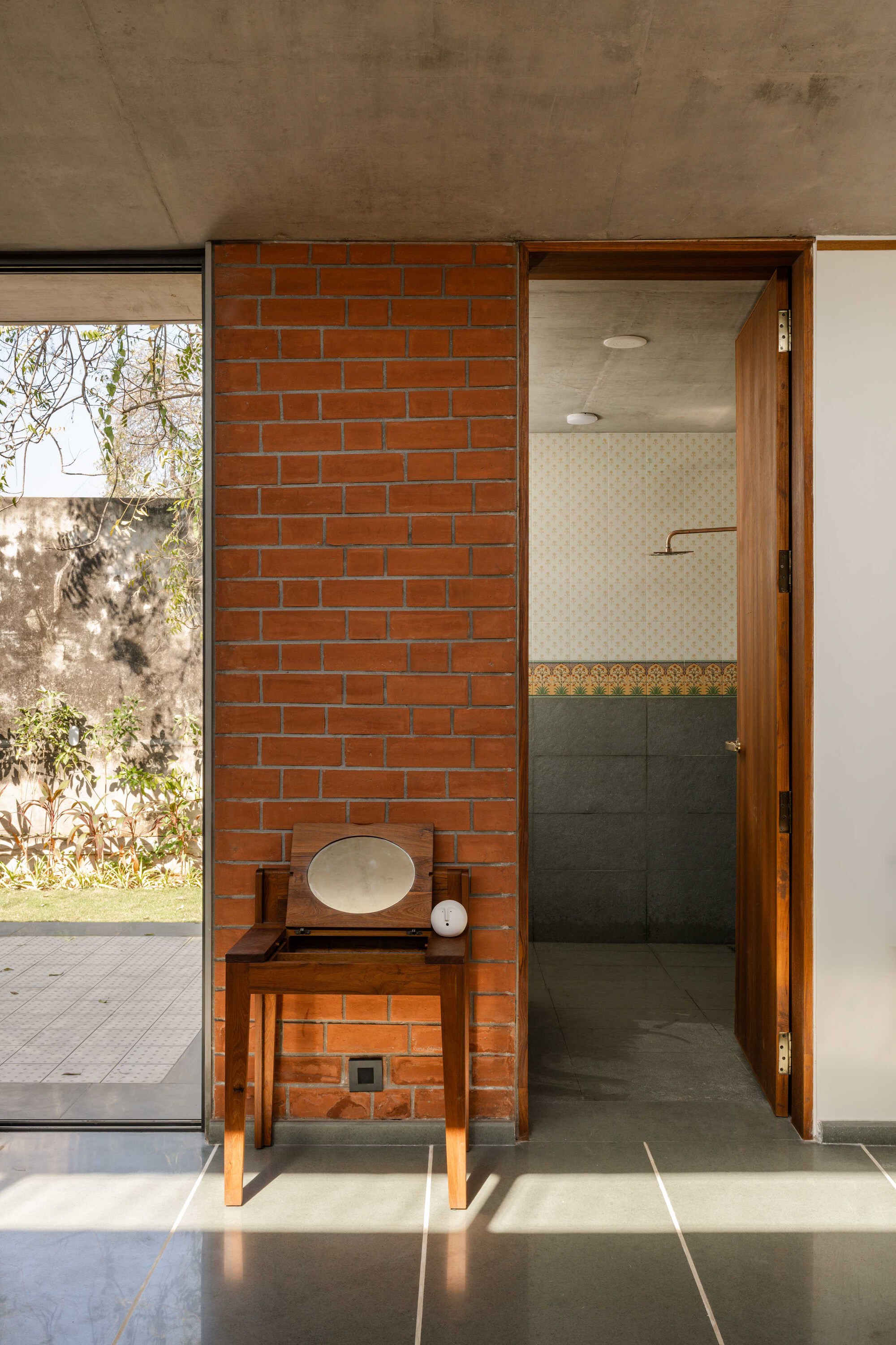 Bathroom entry with red brick wall, timber vanity table, and view to courtyard beyond