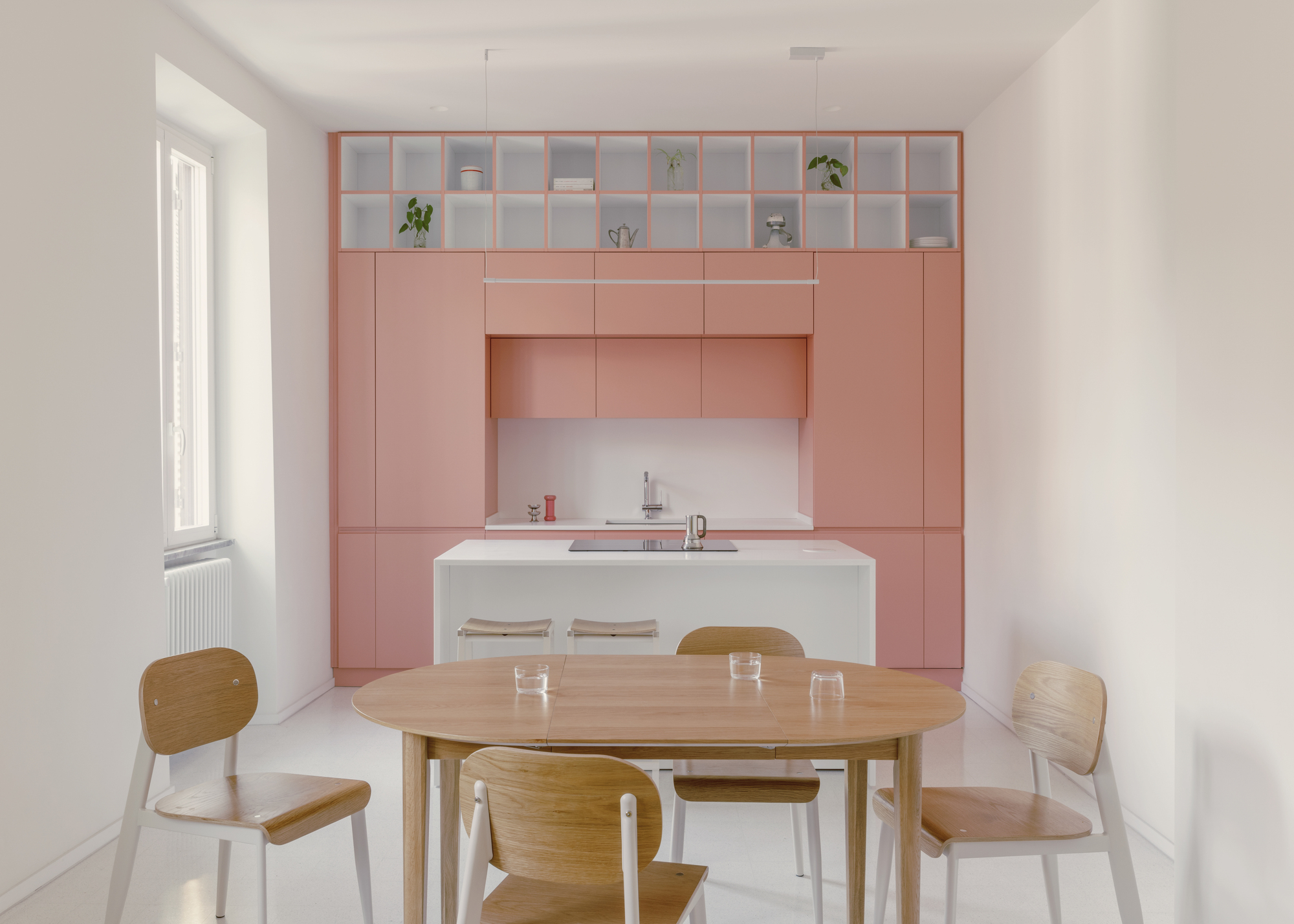 Kitchen with floor-to-ceiling pink joinery and upper glass shelving above a round timber dining table