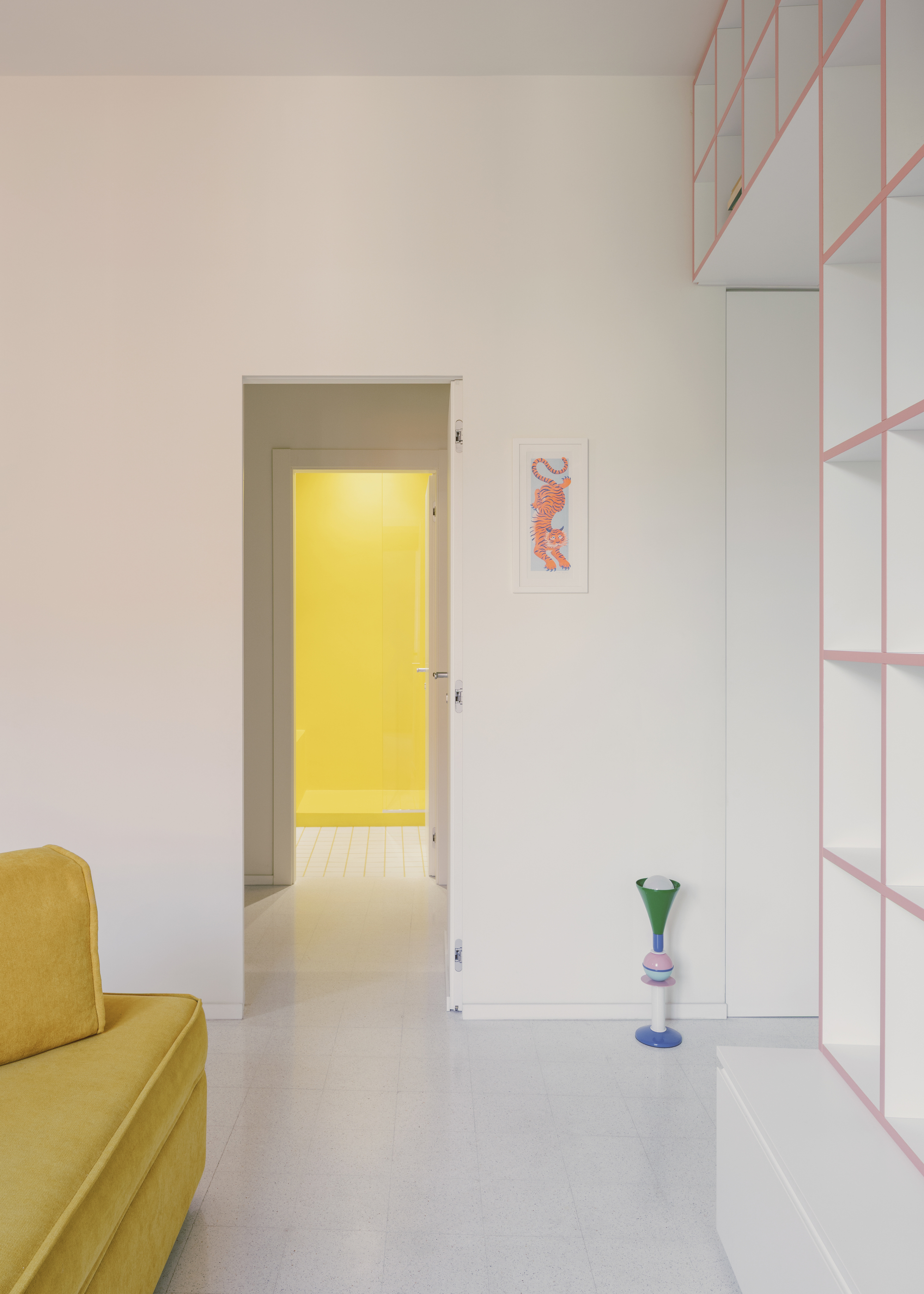 Living room view through doorway to yellow-lit room beyond with pink shelving along the wall