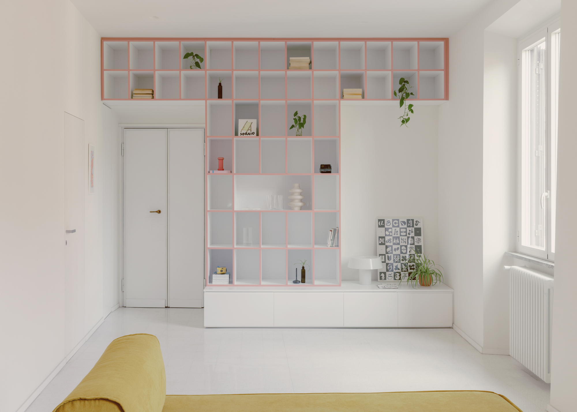 Pink-framed shelving unit with books and plants above white storage cabinetry in bright daylight