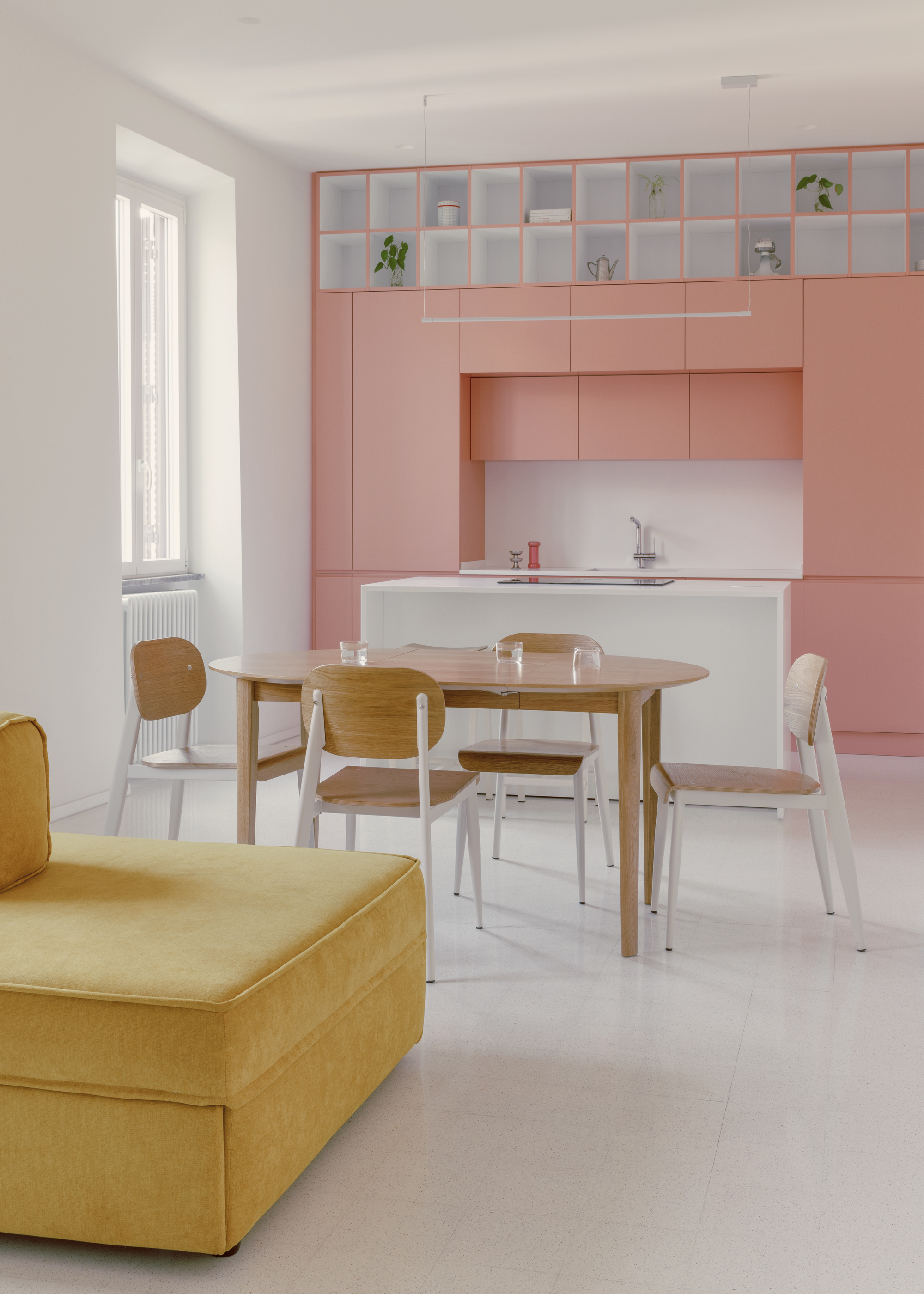 Open-plan kitchen and dining space with pink cabinetry and yellow sofa in morning light
