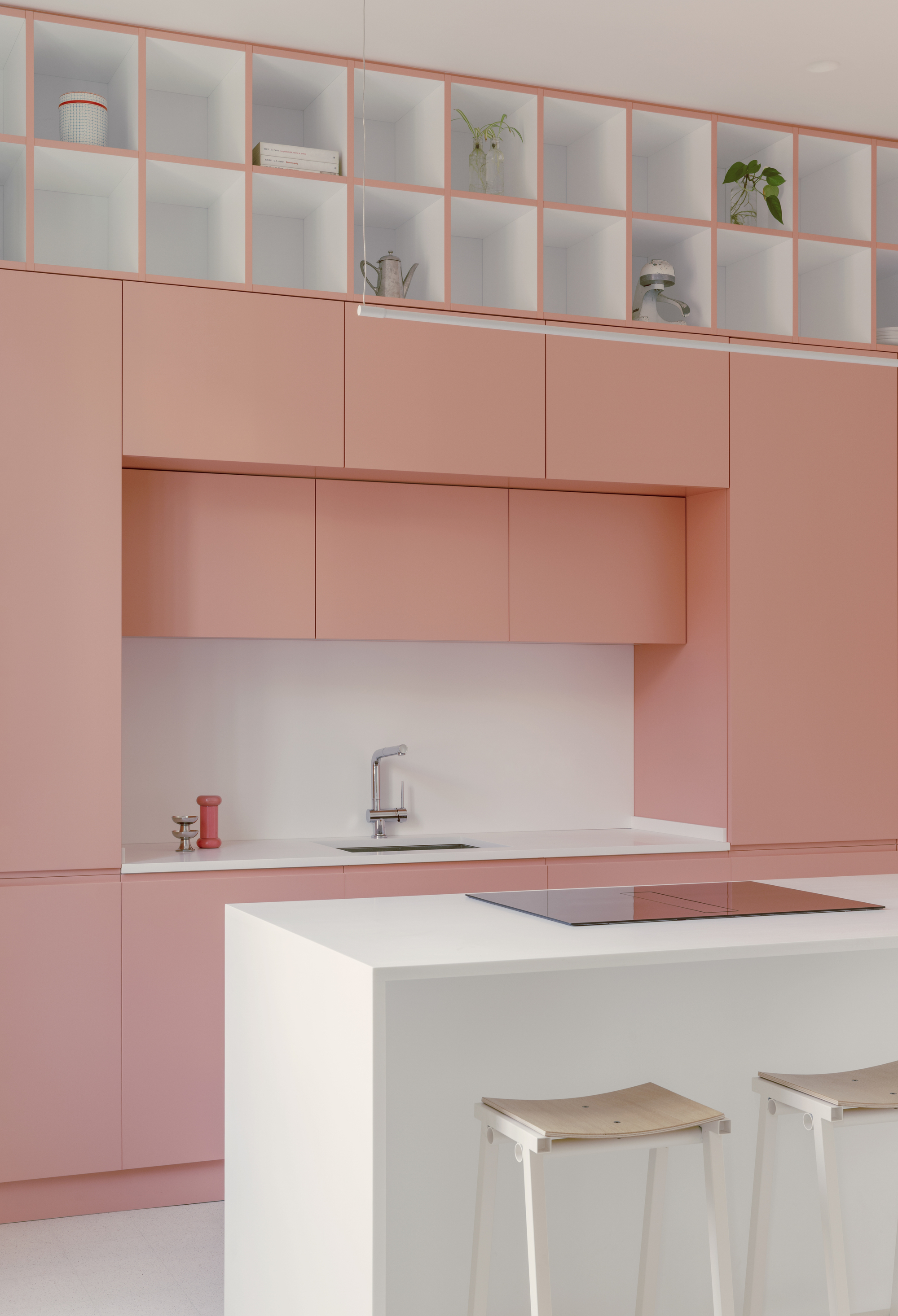 Kitchen with pale pink cabinetry, white island with integrated cooktop, and open shelving above displaying plants