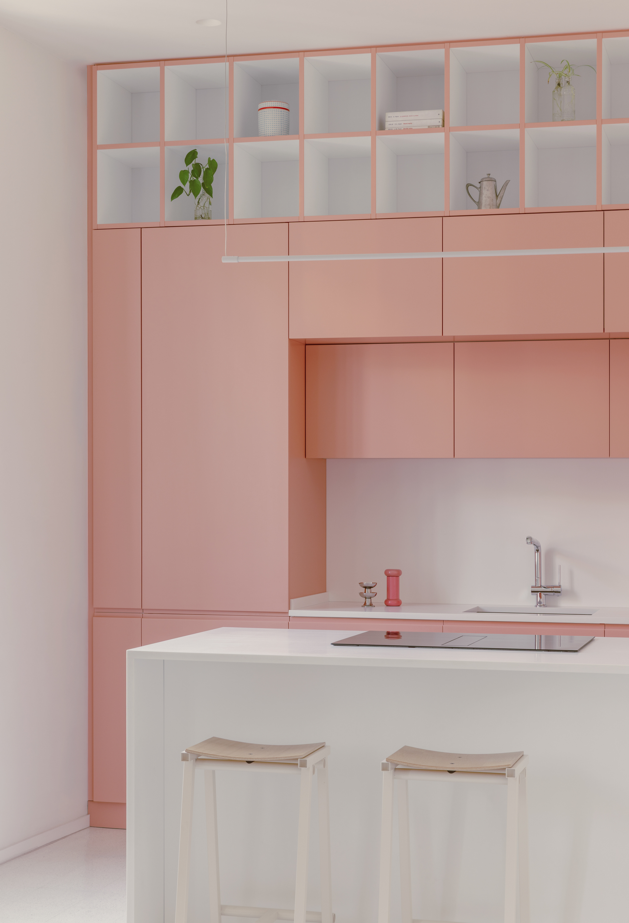 Pink lacquered cabinets surrounding white island with two pale timber stools beneath pendant light