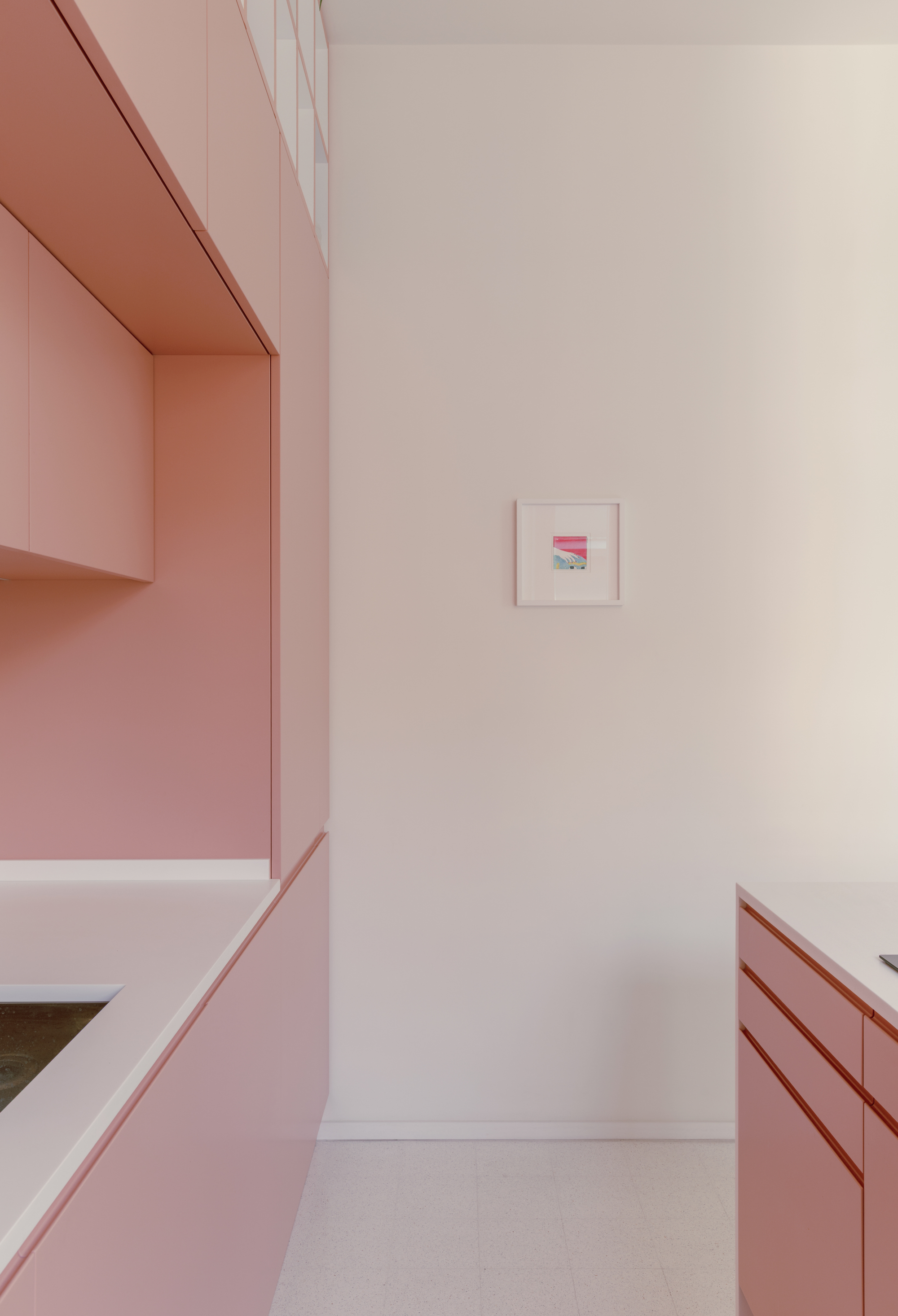 Galley kitchen corridor with pink cabinetry on both sides and small framed artwork on white wall