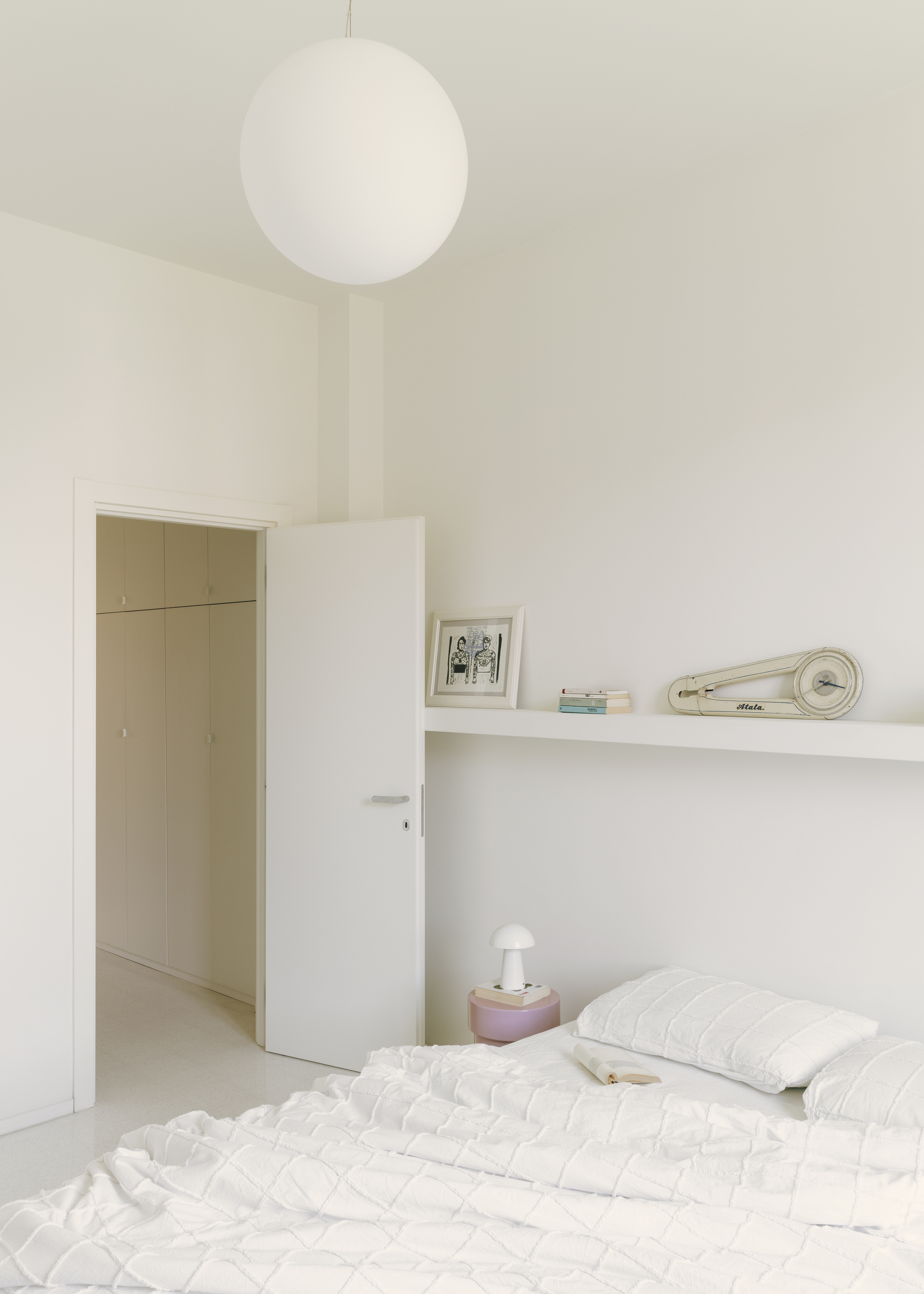 Bedroom with spherical pendant light, open doorway, white shelf and pink cylindrical bedside lamp
